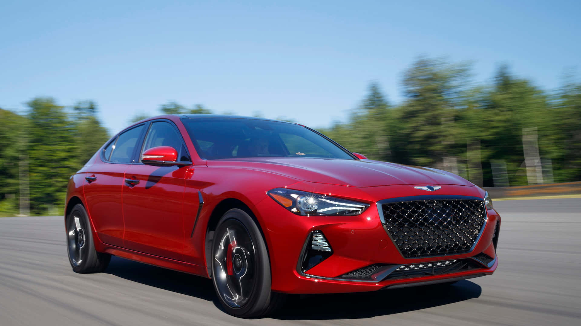 Genesis G70 桌布 壁紙 — 一輛鮮紅色的現代 Genesis 房車在陽光明媚的道路上行駛，背景是模糊的綠色樹木。