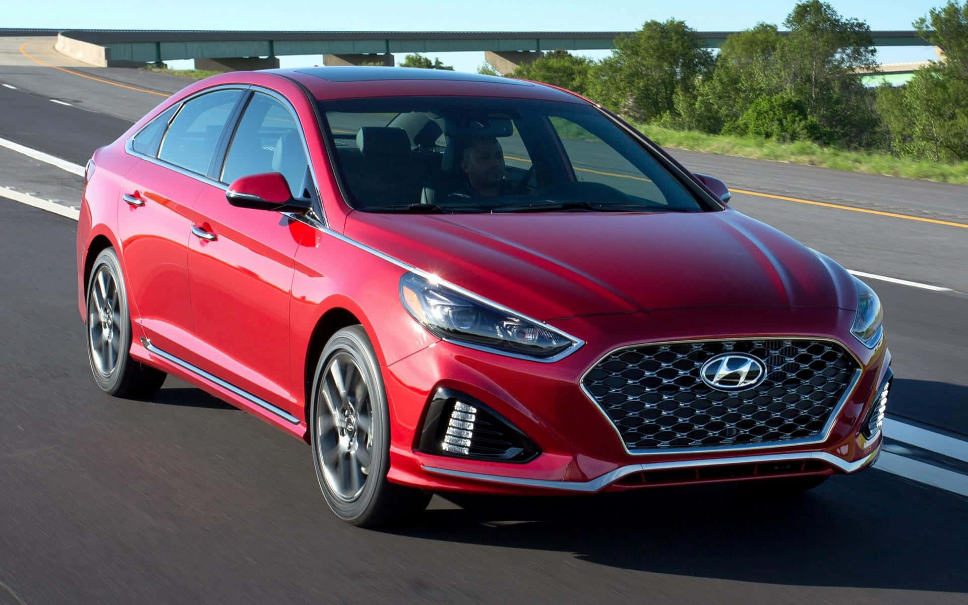 Hyundai Sonata 桌布 壁紙 — 一輛鮮紅色的現代索納塔在陽光明媚的高速公路上行駛，背景有綠樹和橋樑。