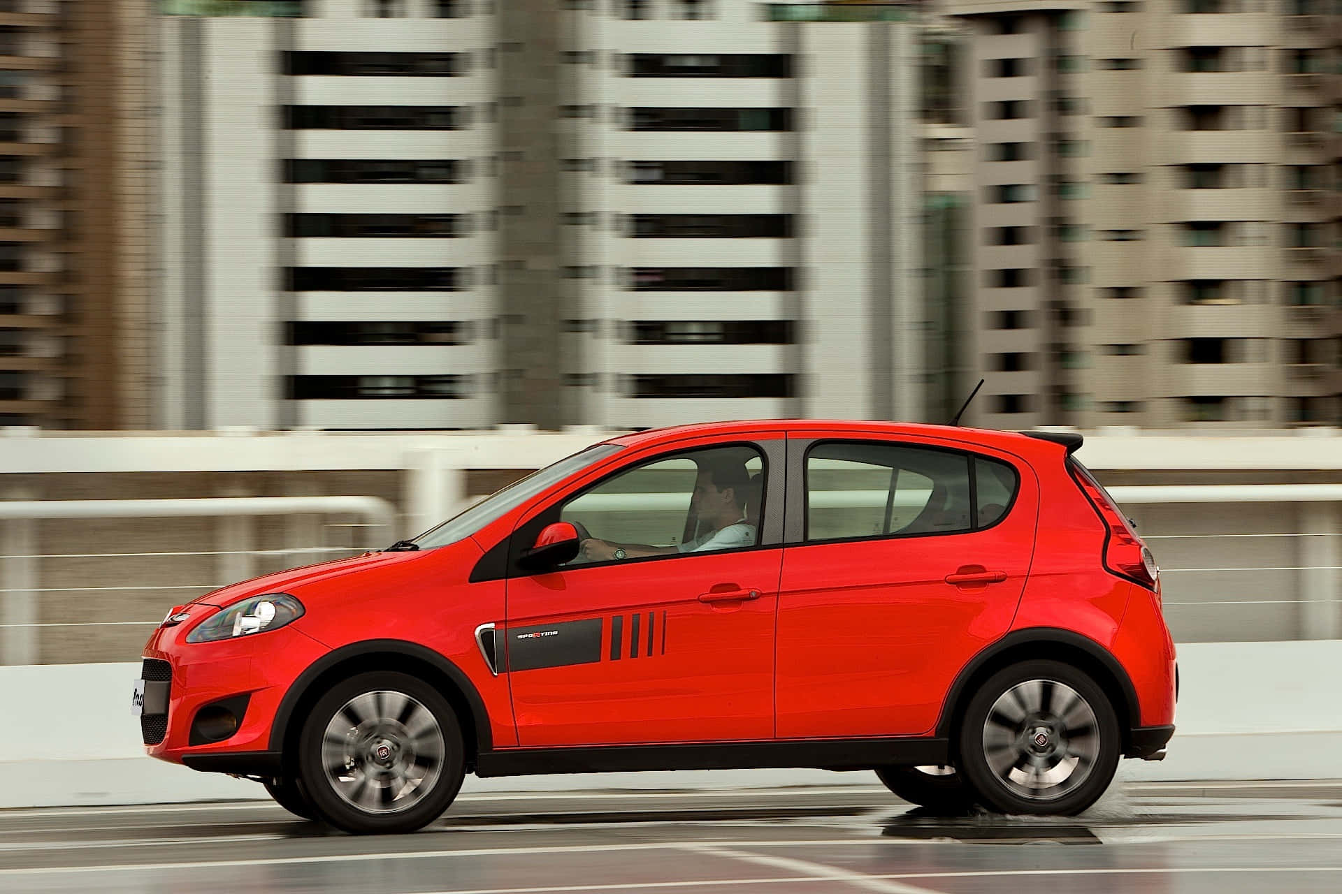 Fiat Palio 桌布 壁紙 — 一輛鮮紅色的緊湊型汽車沿著城市高架橋飛馳，背景是模糊的摩天大樓。