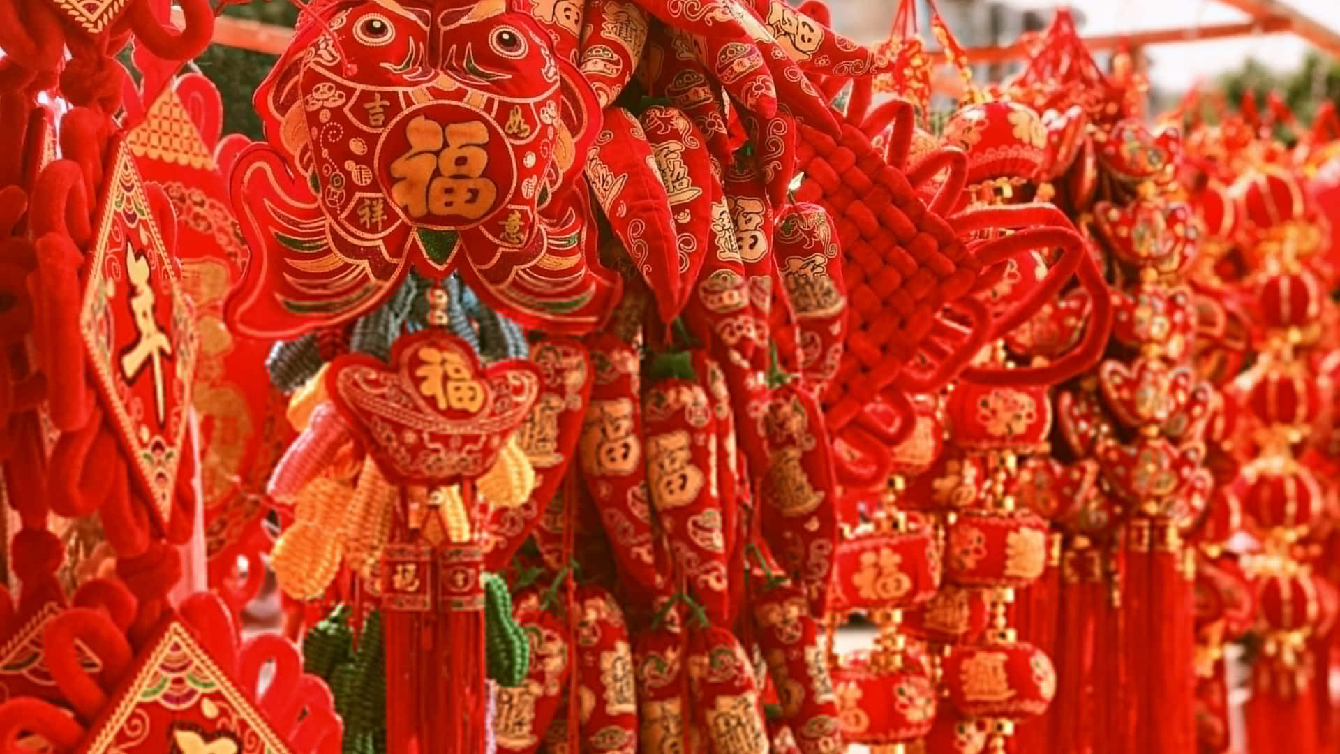  壁紙 — 鮮豔的紅色中國新年裝飾品，帶有金色字元和流蘇，密集地掛在節日市場展示中。