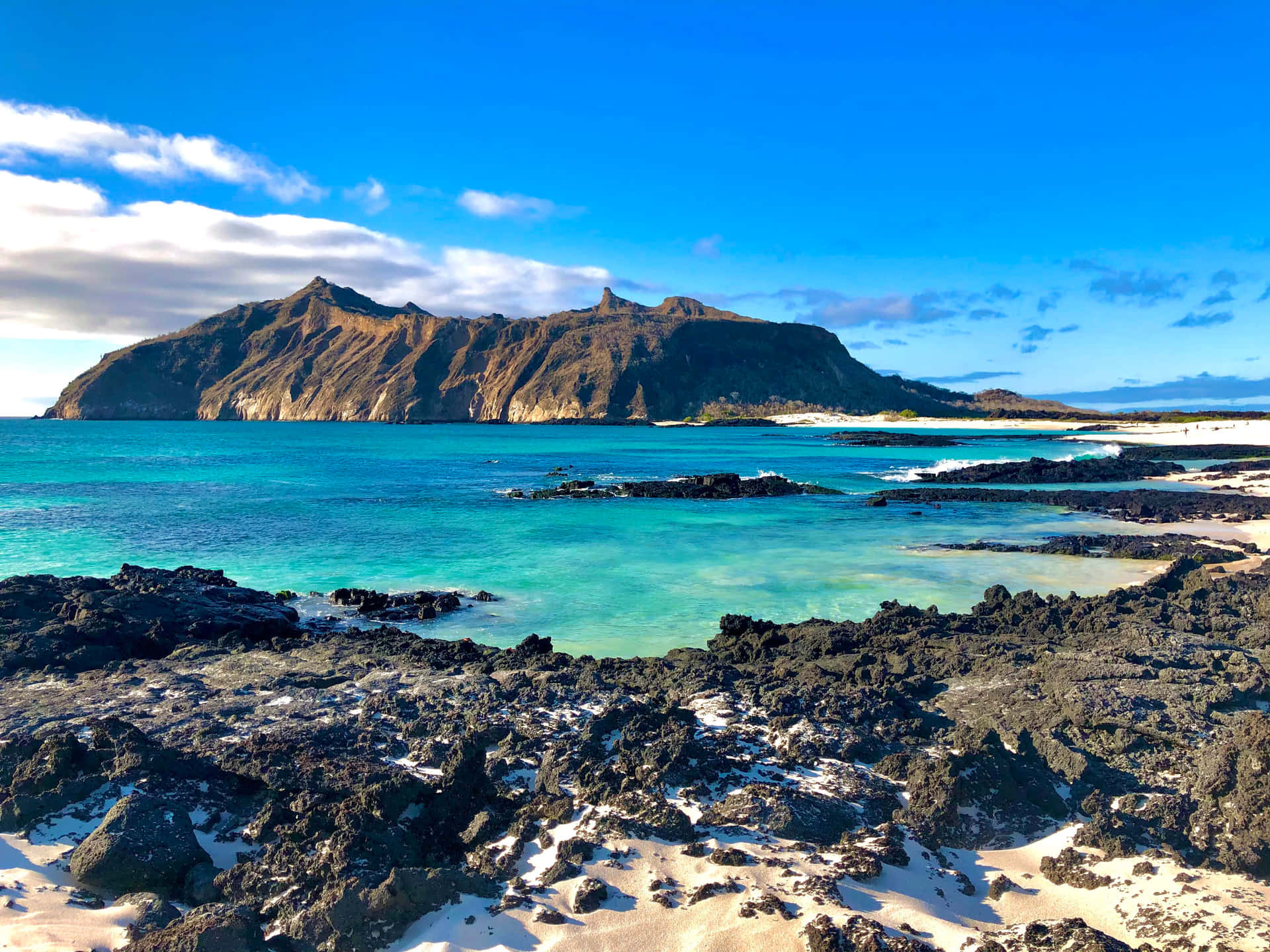  壁紙 — 鮮豔的藍綠色海水拍打著黑色火山岩和白色沙灘，靠近一個崎嶇的山島，天空湛藍。