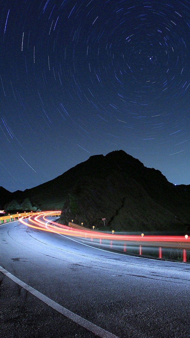 夜晚蜿蜒的山路，帶有星軌和汽車燈光條紋。