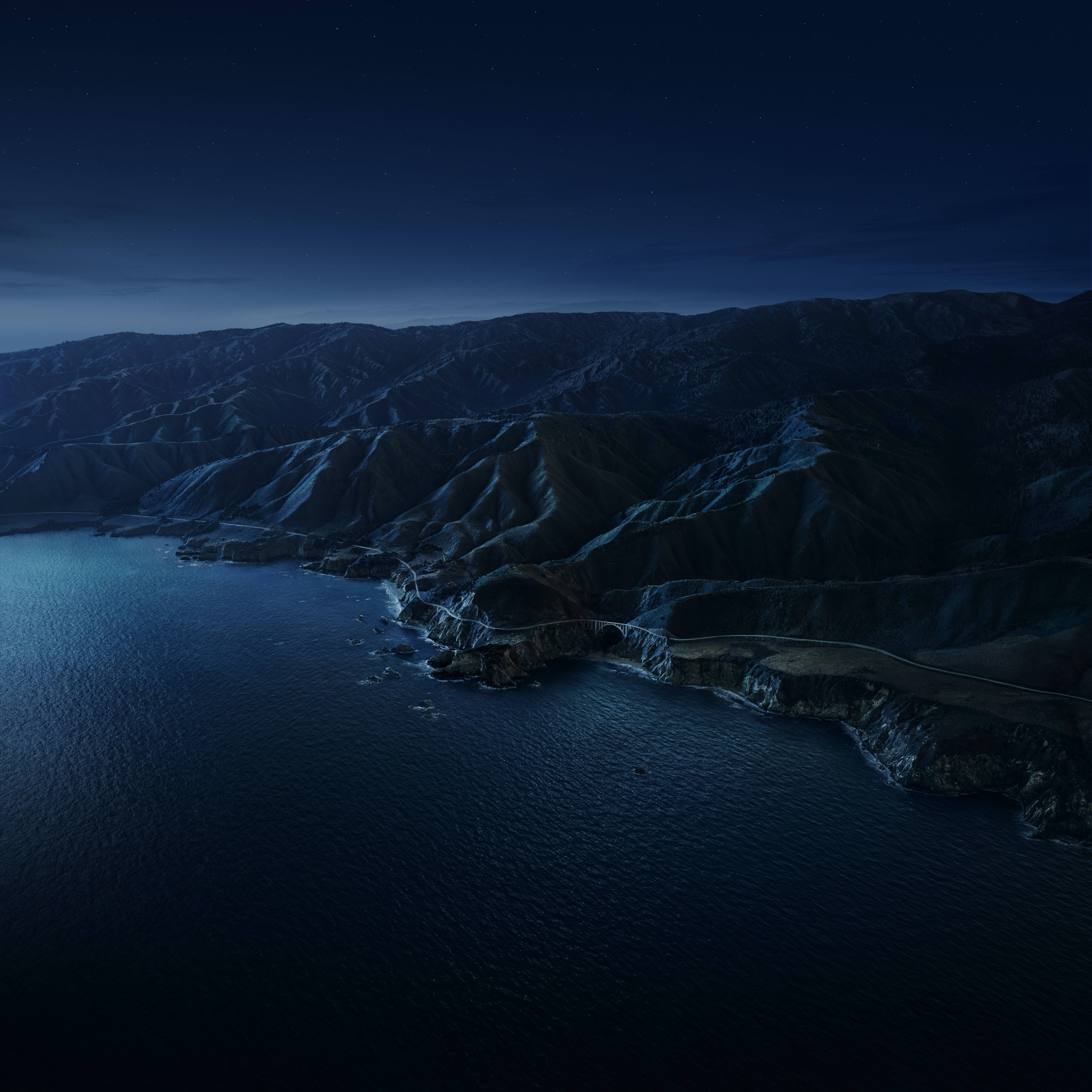 Big Sur夜間海岸 壁紙 — 星空下的夜空俯瞰著一條蜿蜒的海岸公路，緊貼著深藍色的山脈，旁邊是平靜的海洋。