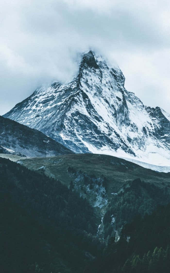  壁紙 — 雄偉的雪山峰頂穿透迷霧雲層，聳立在黑暗的森林山谷之上。