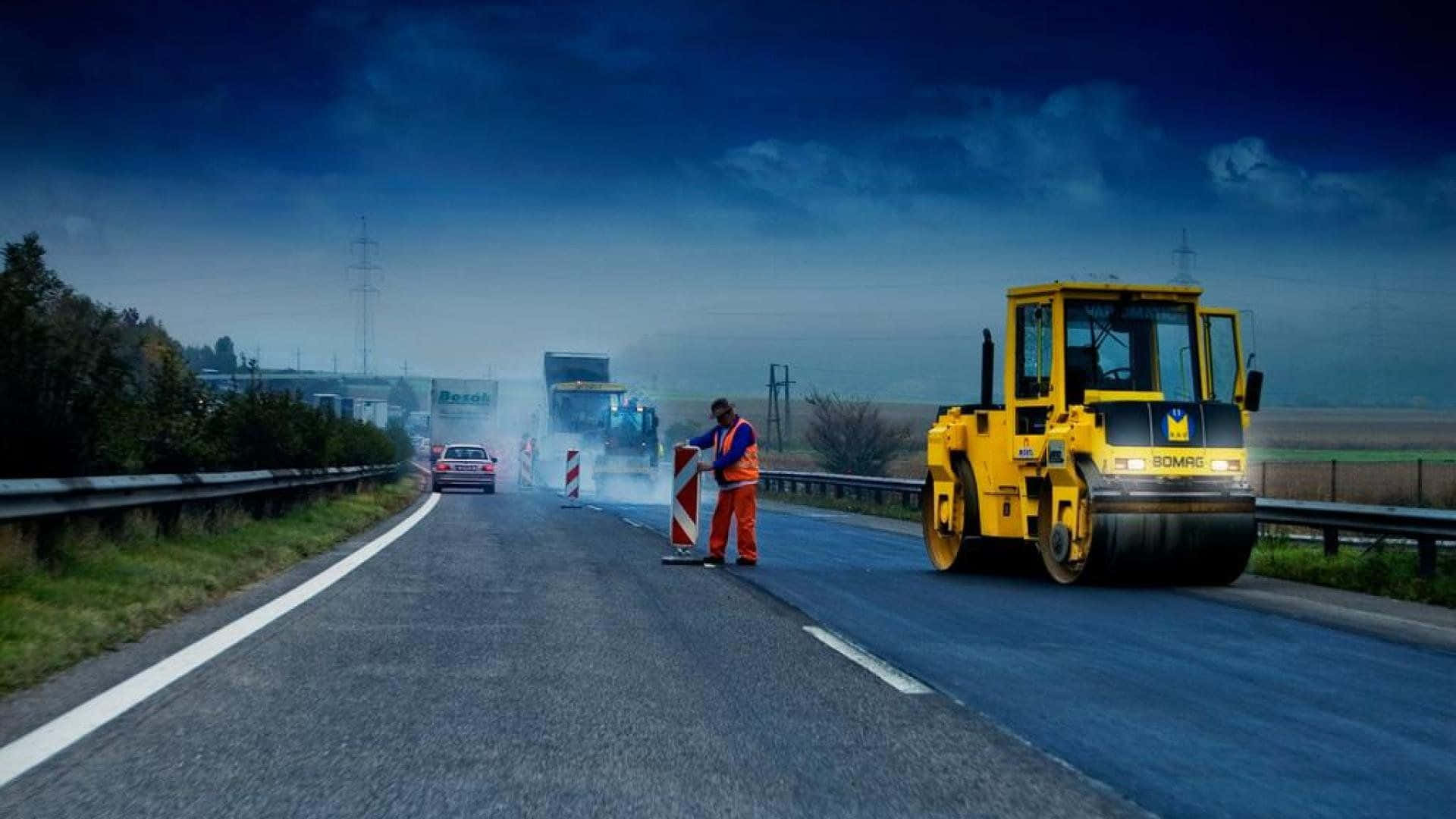 修路工人在有霧的高速公路上，在蒸汽壓路機附近指揮交通，黃昏時分。