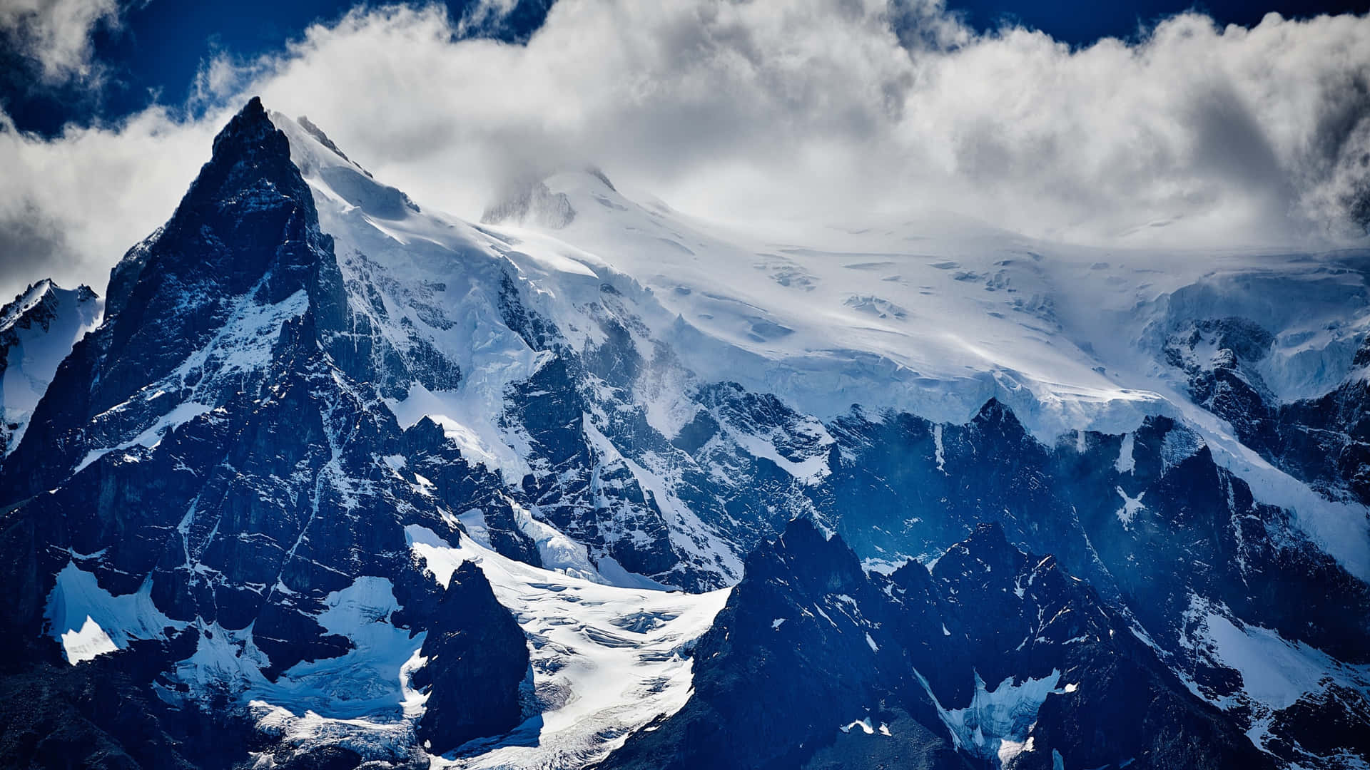 雪山頂峰聳立於雲層之上，深藍色天空