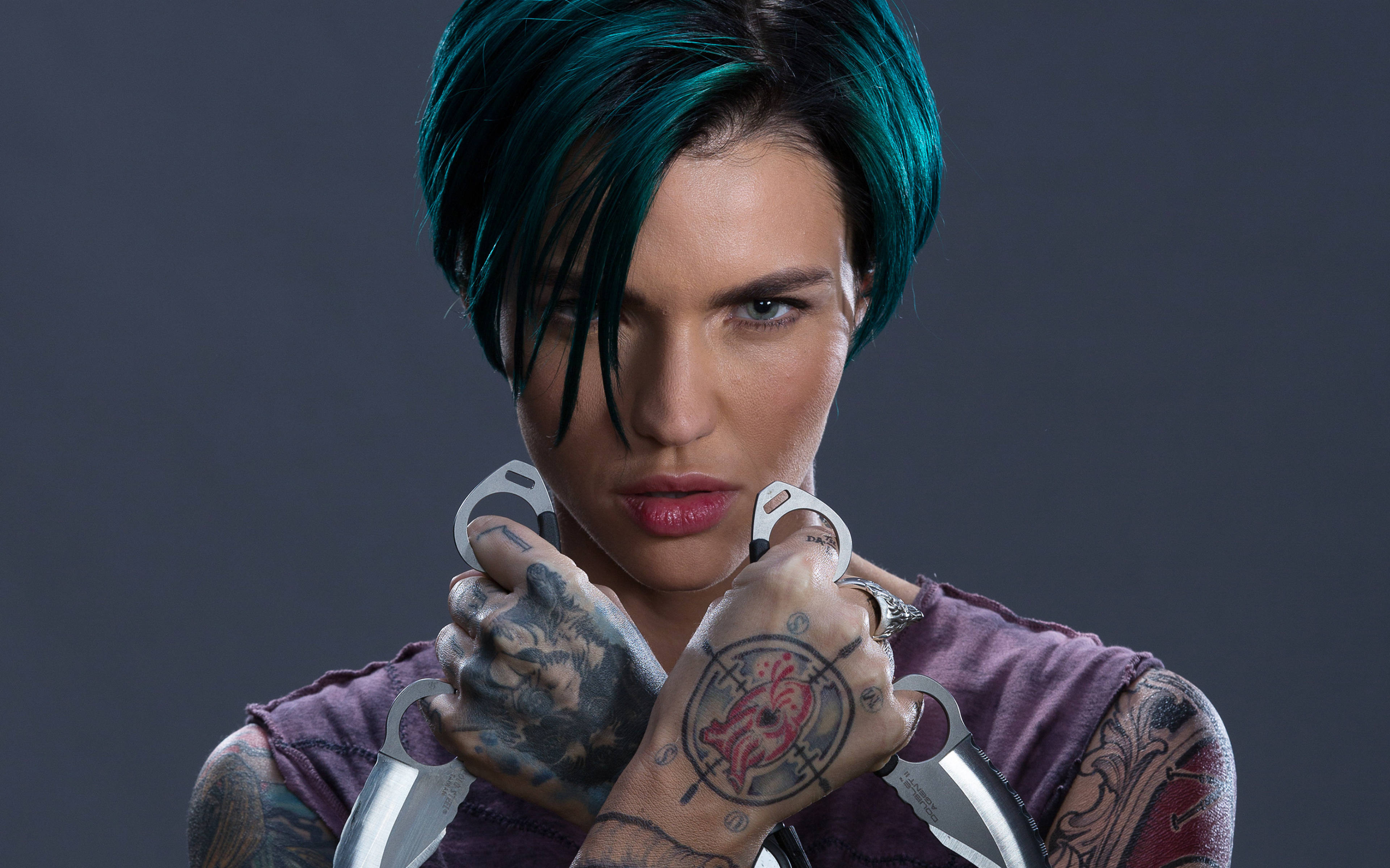 魯比·羅斯出演《XXX：重返Xander Cage》 壁紙 — 一個兇猛的女人，擁有青色頭髮和紋身，在深灰色背景下握著兩把飛刀。