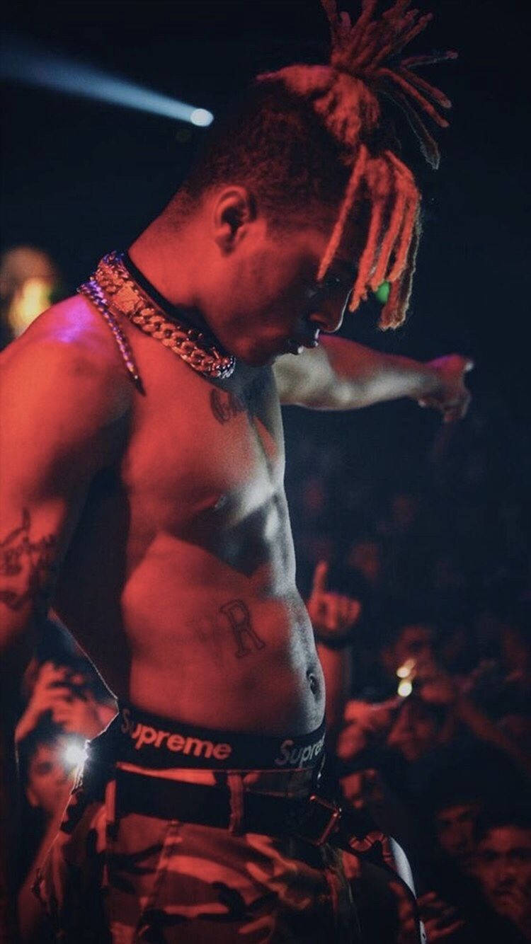 無上衣 XXXTentacion 美學 壁紙 — 一個赤裸上身、留著雷鬼辮和紋身的男人，在紅色燈光下，身後有群眾，在舞台上表演。