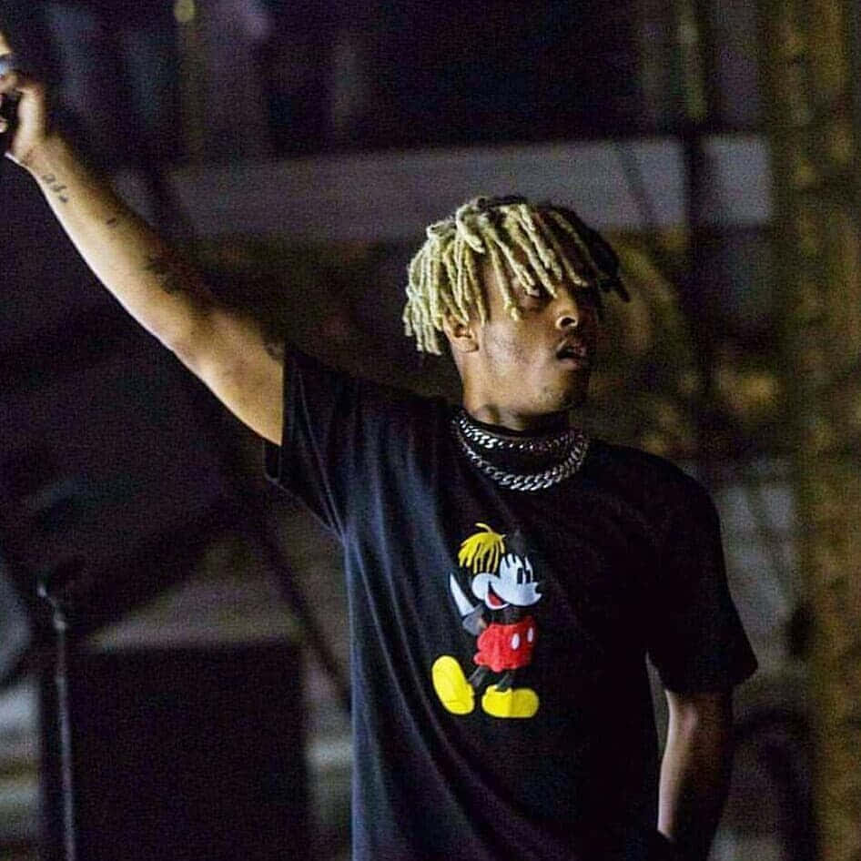 Xxxtentacion 米奇T恤頭像 壁紙 — 一名金髮辮男子在昏暗的夜間燈光下舉起手臂，身穿黑色米奇老鼠T恤。