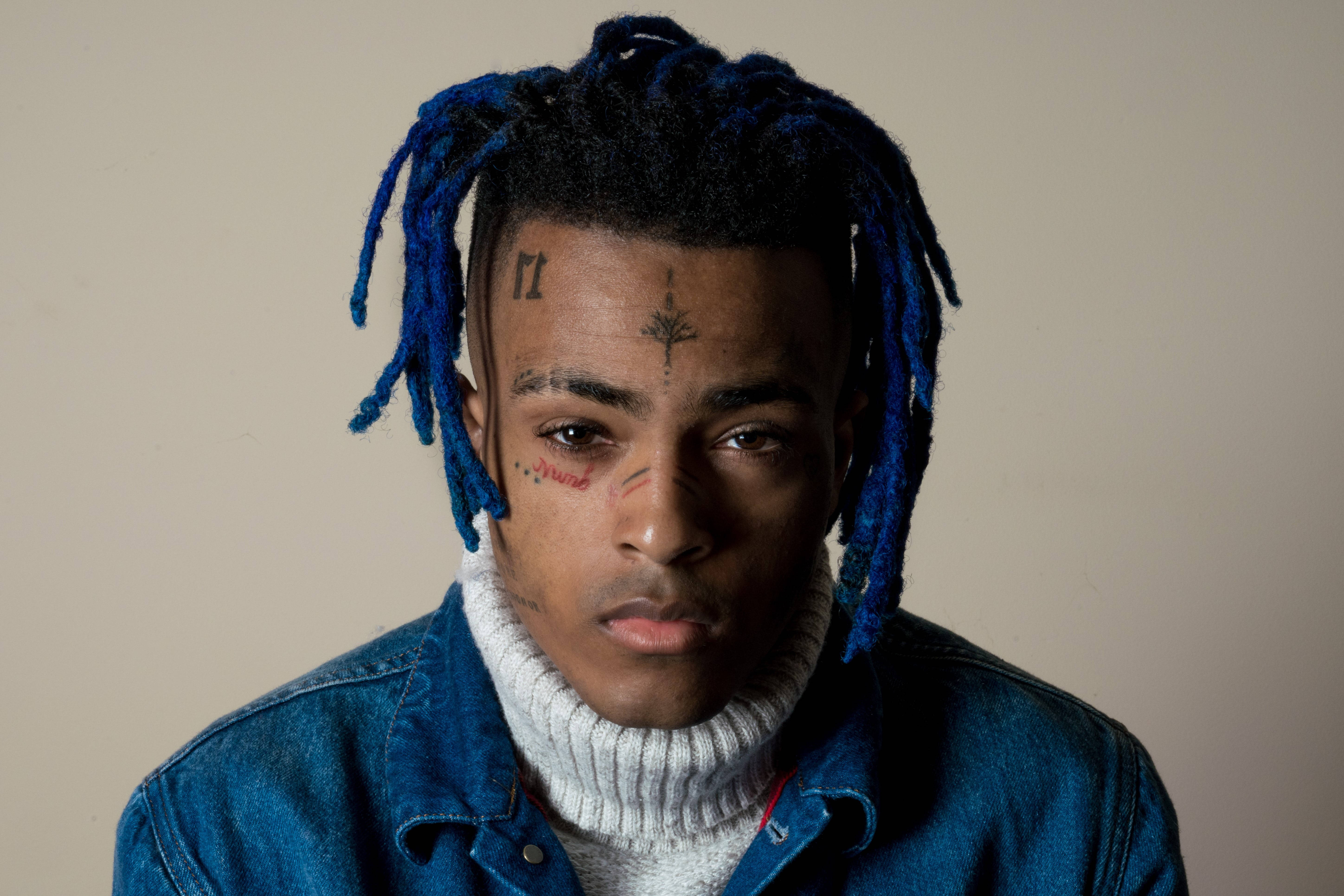 XXXTentacion 男性面部 壁紙 — 一名年輕男子擁有充滿活力的藍色辮子頭和臉部紋身，穿著白色高領毛衣外搭牛仔外套，凝視著鏡頭。