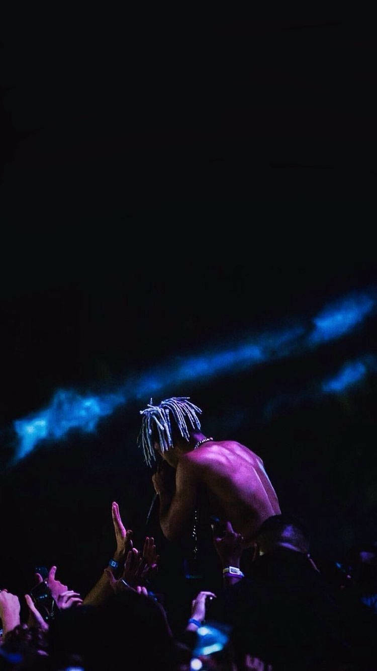 XXXTentacion美學現場演出 壁紙 — 一位赤裸上身、編髮的表演者在藍色舞台燈光下對著麥克風唱歌，粉絲們在黑暗中伸手向他。