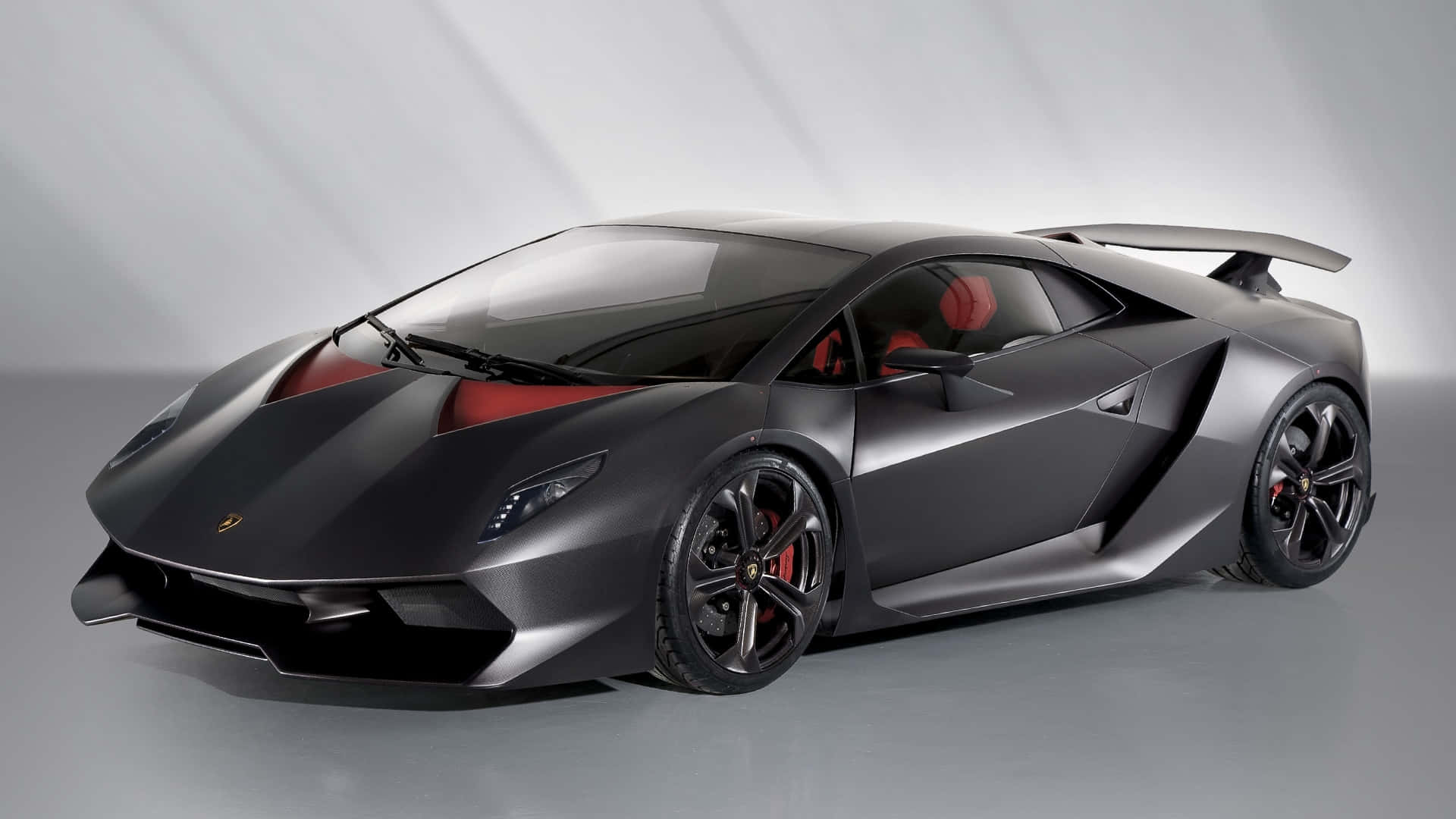 Lamborghini Sesto Elemento 桌布 壁紙 — 一輛時尚的啞光黑色林寶堅尼跑車，帶有紅色點綴和黑色輪圈，擺放在簡約的攝影棚環境中。