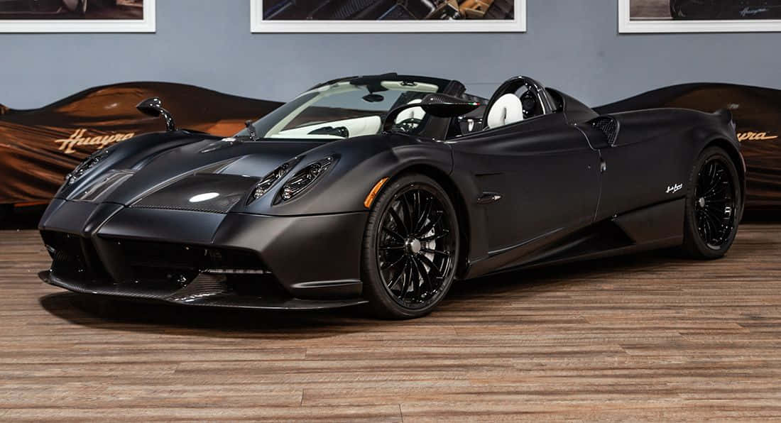 Pagani Zonda C12 Roadster 桌布 壁紙 — 一輛線條流暢的啞光黑色帕加尼Huayra敞篷跑車，配白色內飾，停放在豪華展廳的木地板上。
