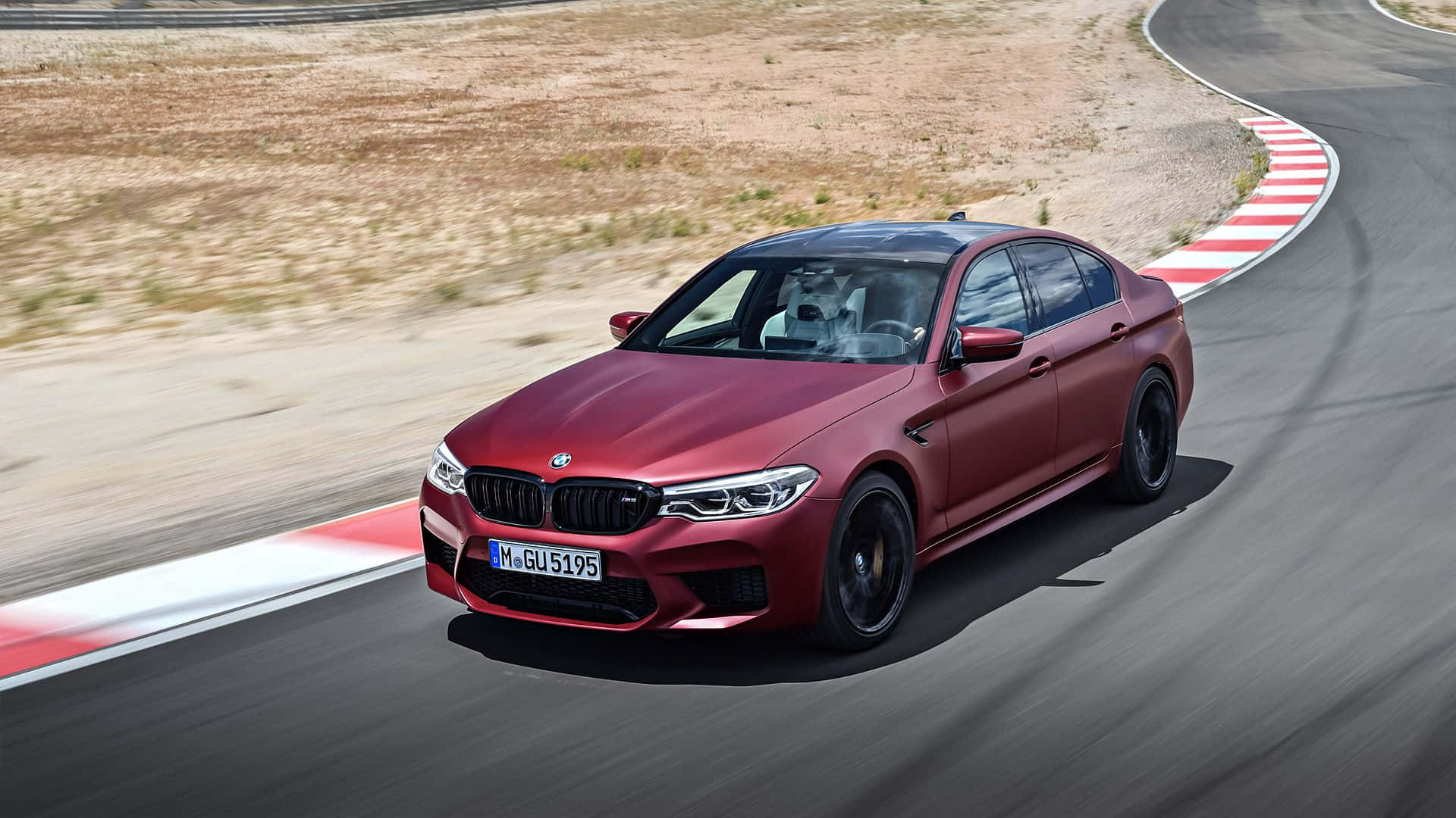 Bmw M5 桌布 壁紙 — 一輛啞光紅色BMW M5房車在賽道上以模糊動態和紅白路緣石激進過彎。