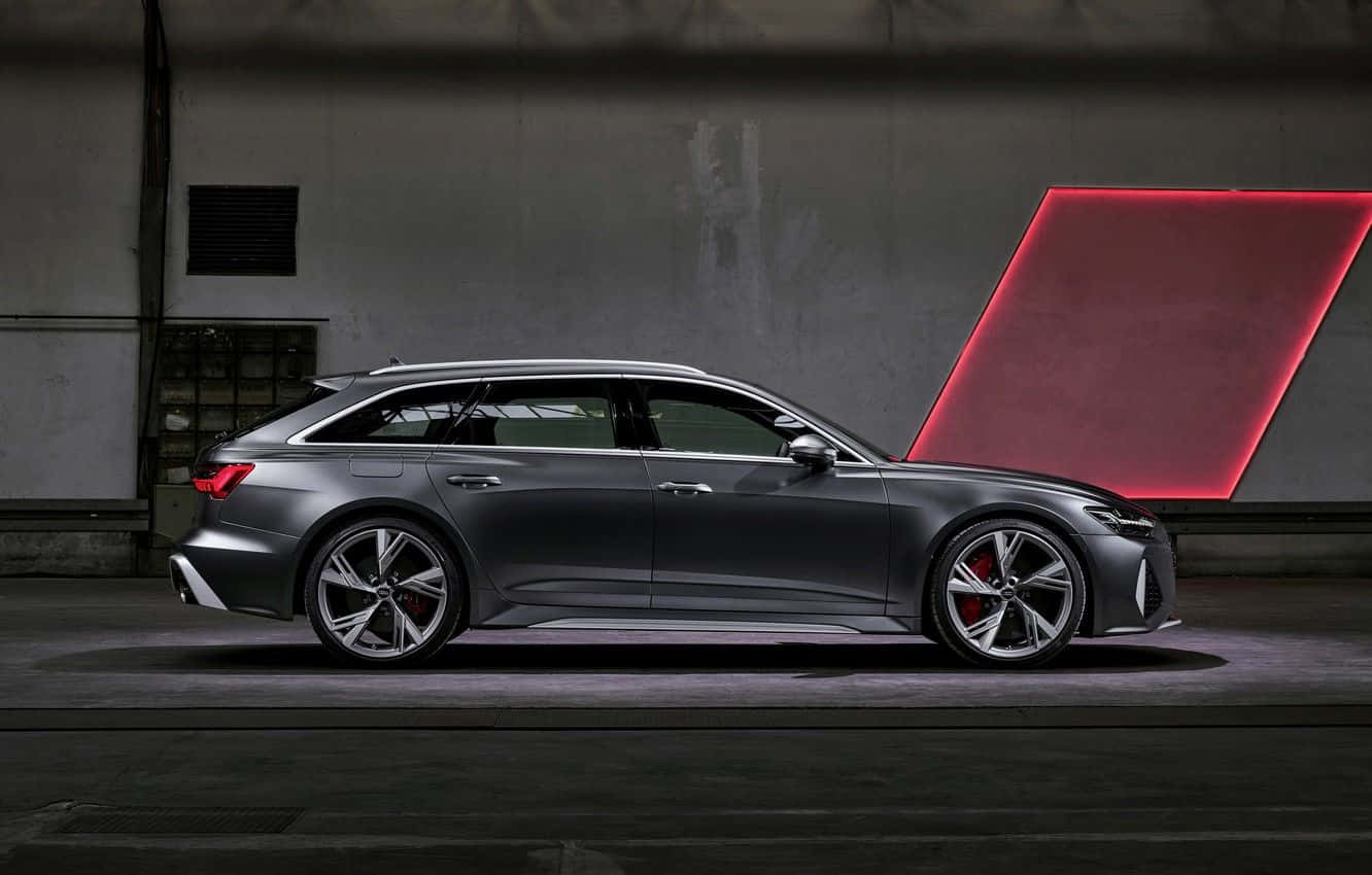 Audi Rs6 桌布 壁紙 — 一輛時尚的啞光灰色奧迪RS6 Avant旅行車在昏暗的工業車庫中展示，背後有一個發光的紅色幾何燈板。