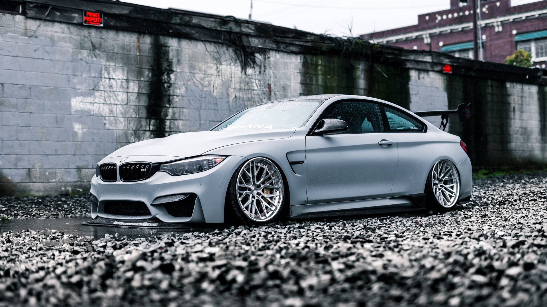 啞光銀色BMW M4雙門跑車停放在碎石上，靠近混凝土牆。
