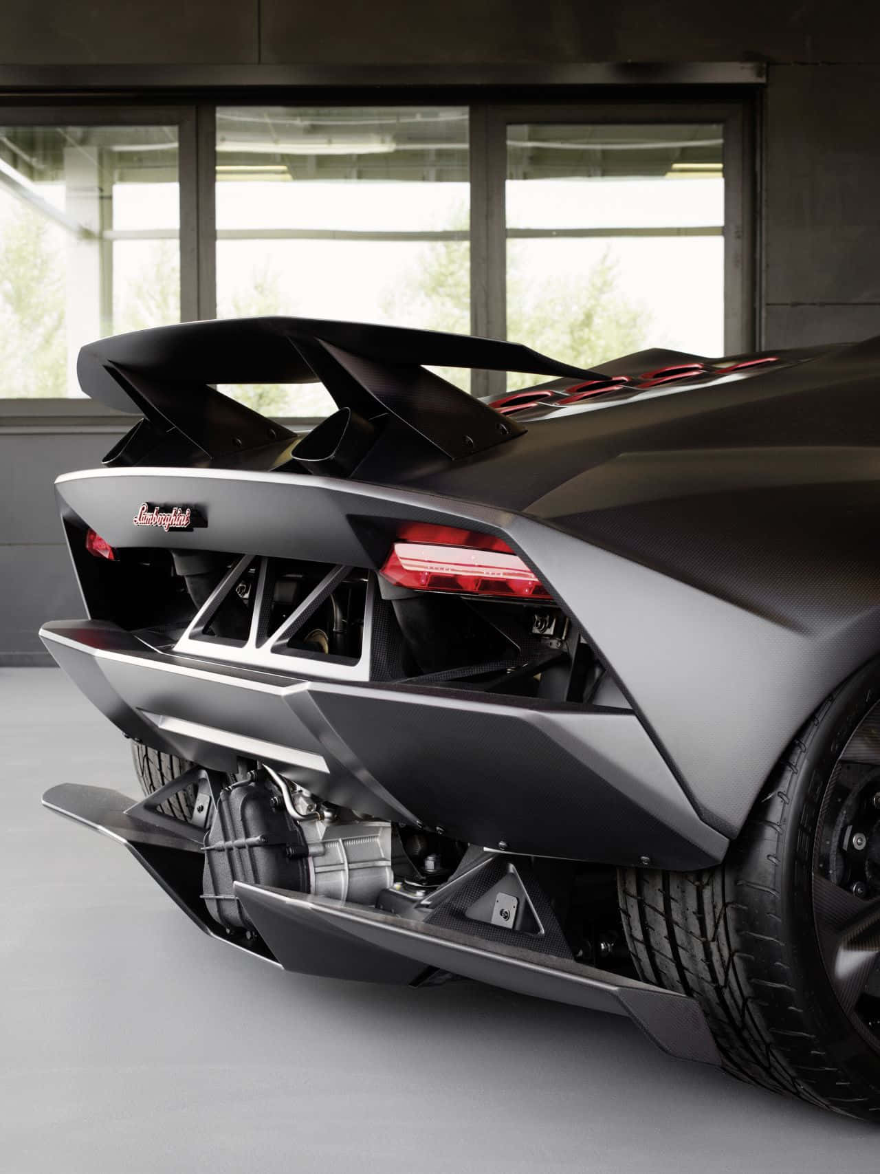 Lamborghini Sesto Elemento 桌布 壁紙 — 一輛啞光黑色的林寶堅尼跑車，引擎外露，紅色尾燈，停放在室內大窗附近。