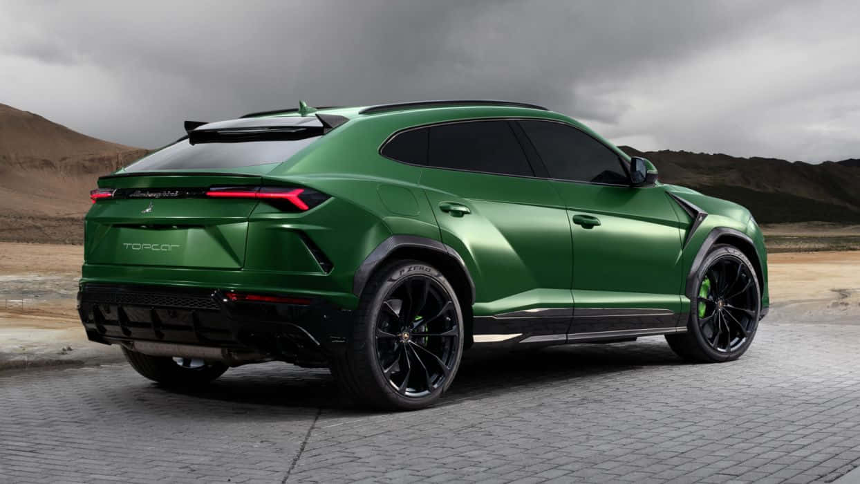 Lamborghini Urus 桌布 壁紙 — 一輛啞光綠色的林寶堅尼 Urus 停泊在鋪砌路面上，天空多雲，背景是乾燥的山丘。