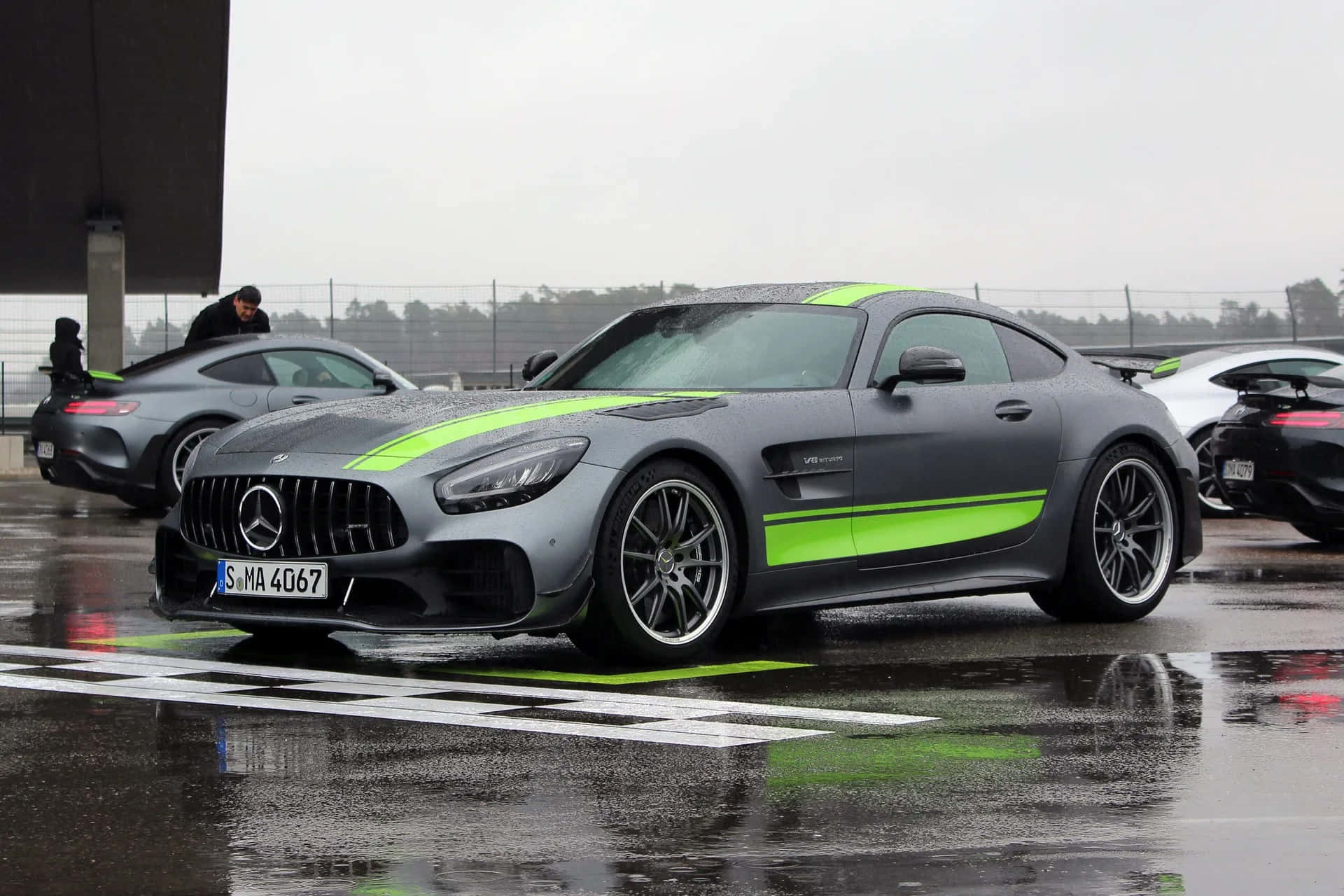  壁紙 — 一架啞光灰色梅賽德斯-AMG GT R，帶有螢光綠色條紋，停在潮濕賽道格柵上，天空多雲。