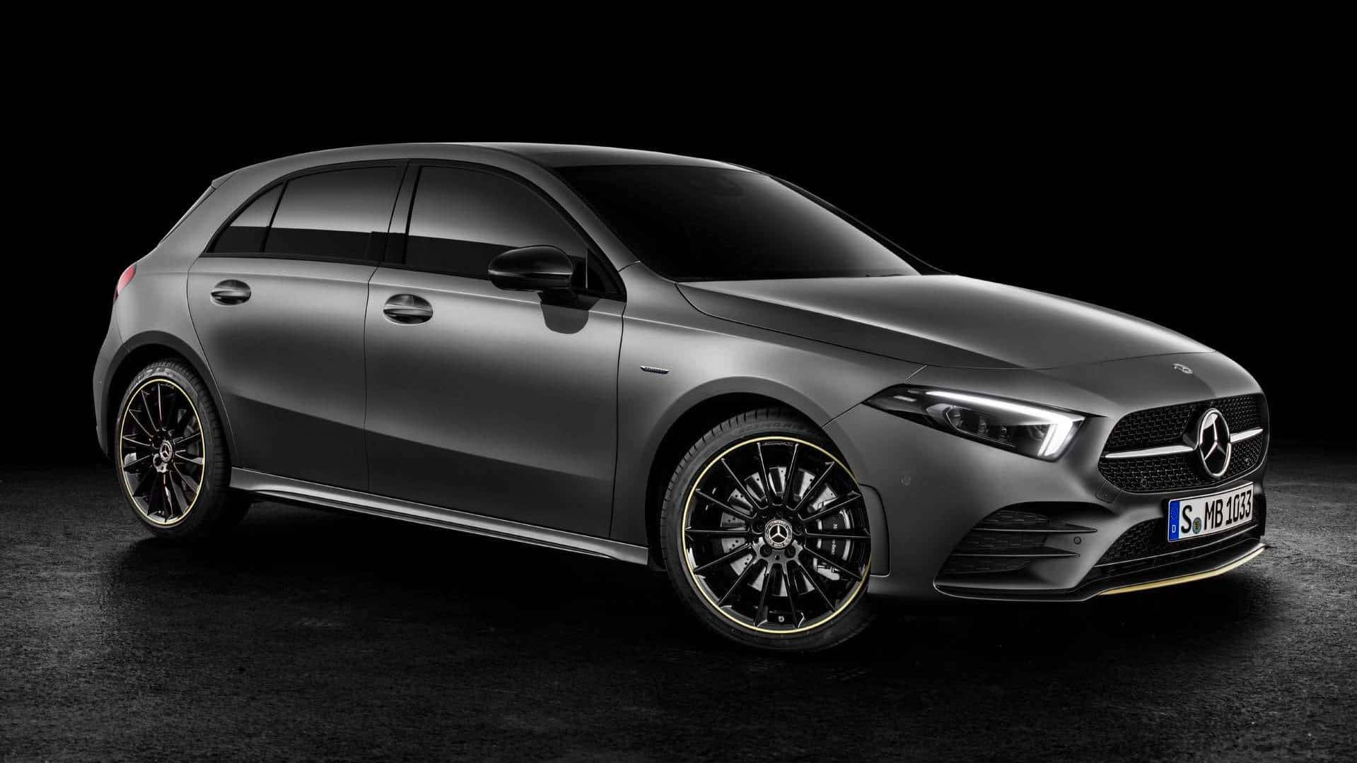 Mercedes Benz A-class 桌布 壁紙 — 一輛時尚的啞光灰色平治A-Class掀背車，配備黑色輪圈和金色飾邊，在深色工作室背景中展示。