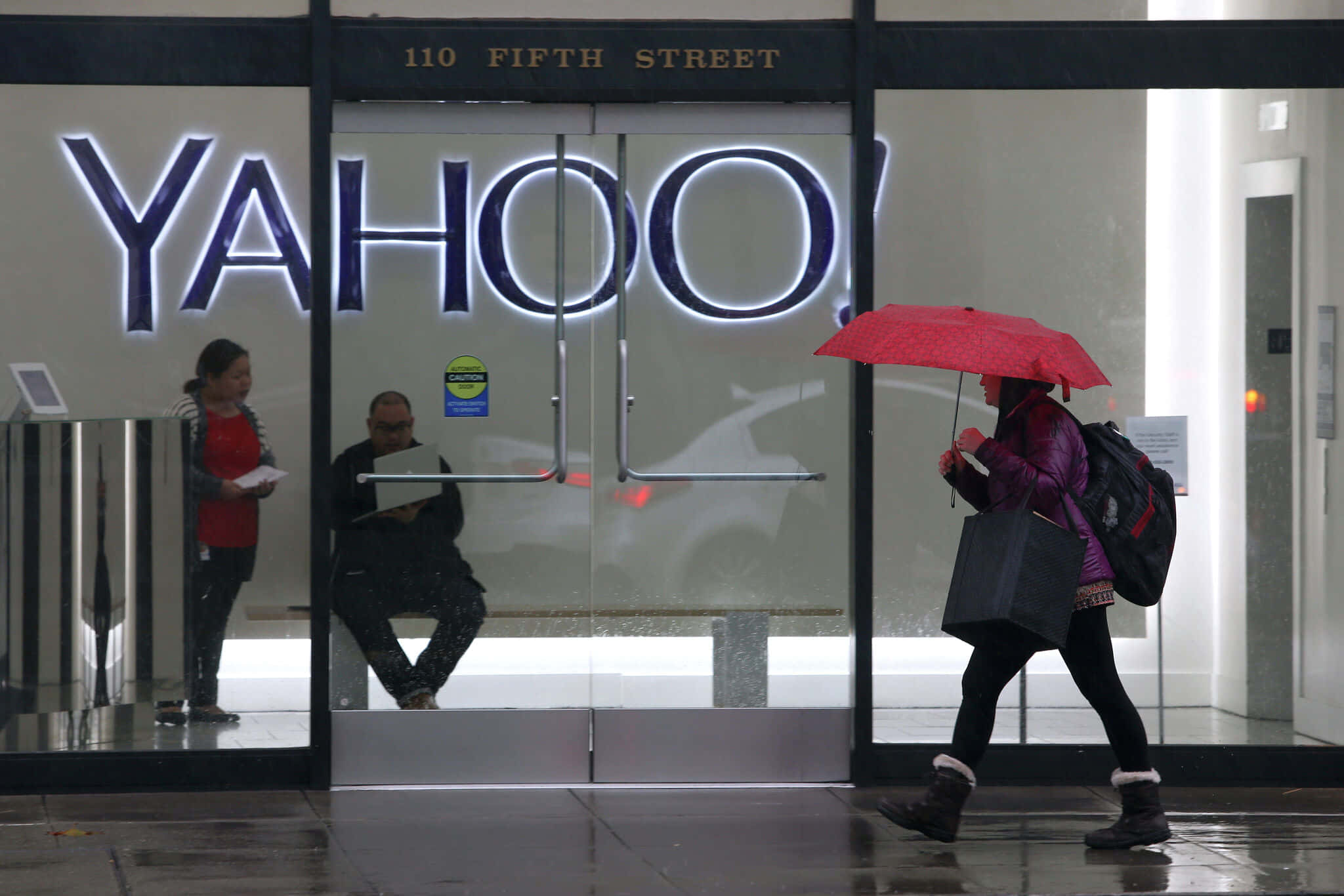 為現代時代釋放Yahoo!的潛力 壁紙 — 一個人在下雨天撐著紅色雨傘走過玻璃幕牆的Yahoo辦公大樓。