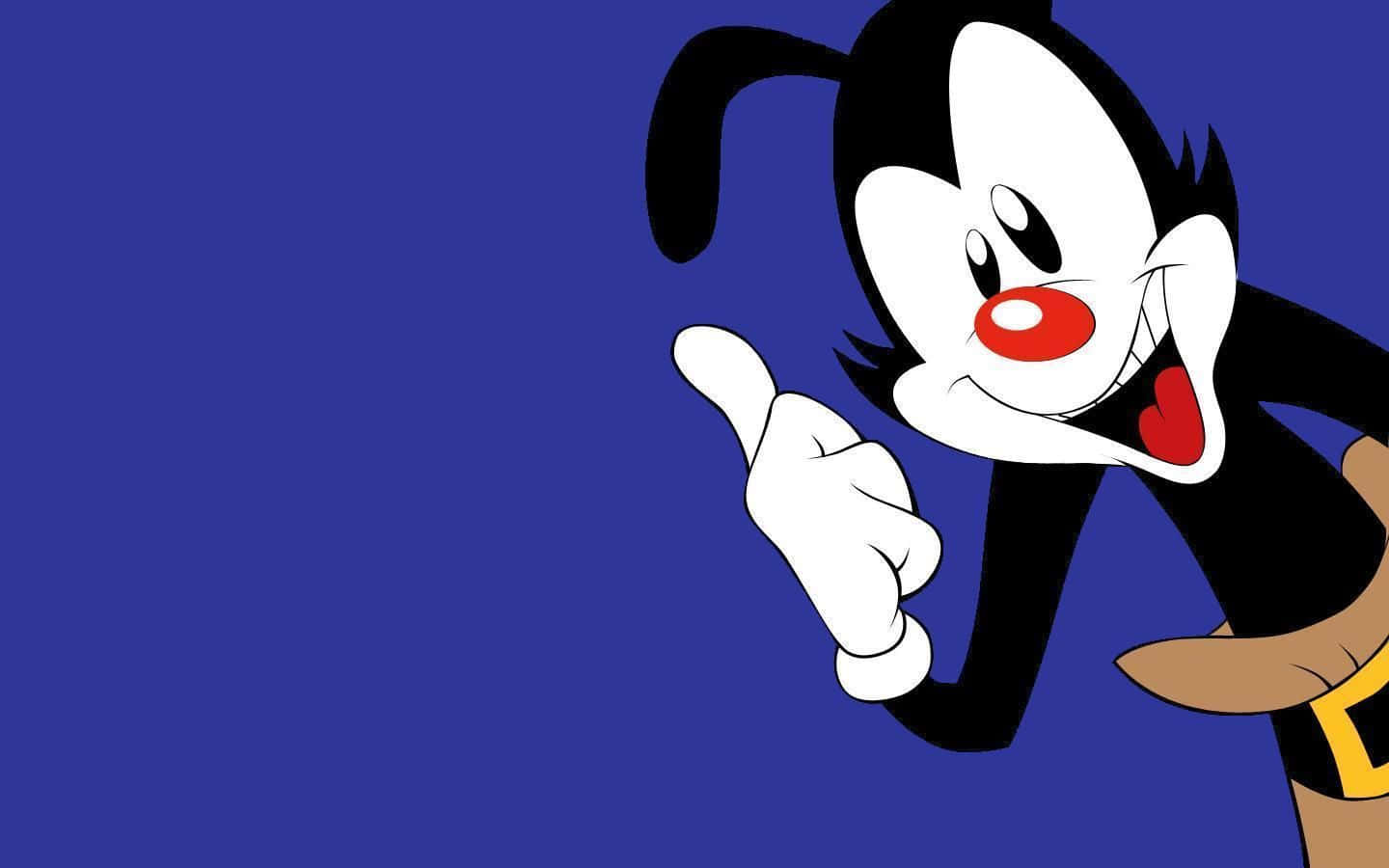 Yakko、Wakko與Dot登台表演 壁紙 — 一個黑白毛髮、紅鼻子、咧嘴大笑的卡通角色，在純藍色背景前開心地指著。
