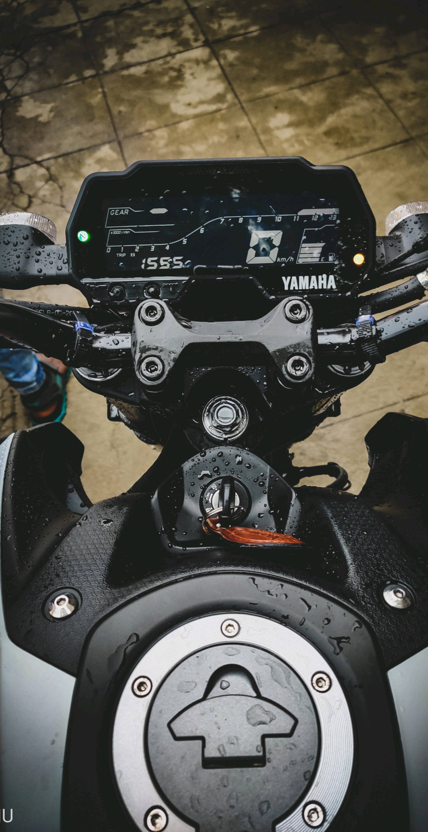 yamaha mt 15 桌布 壁紙 — Yamaha電單車潮濕的儀表板和油箱特寫，雨滴在黑色和銀色表面上閃閃發光。