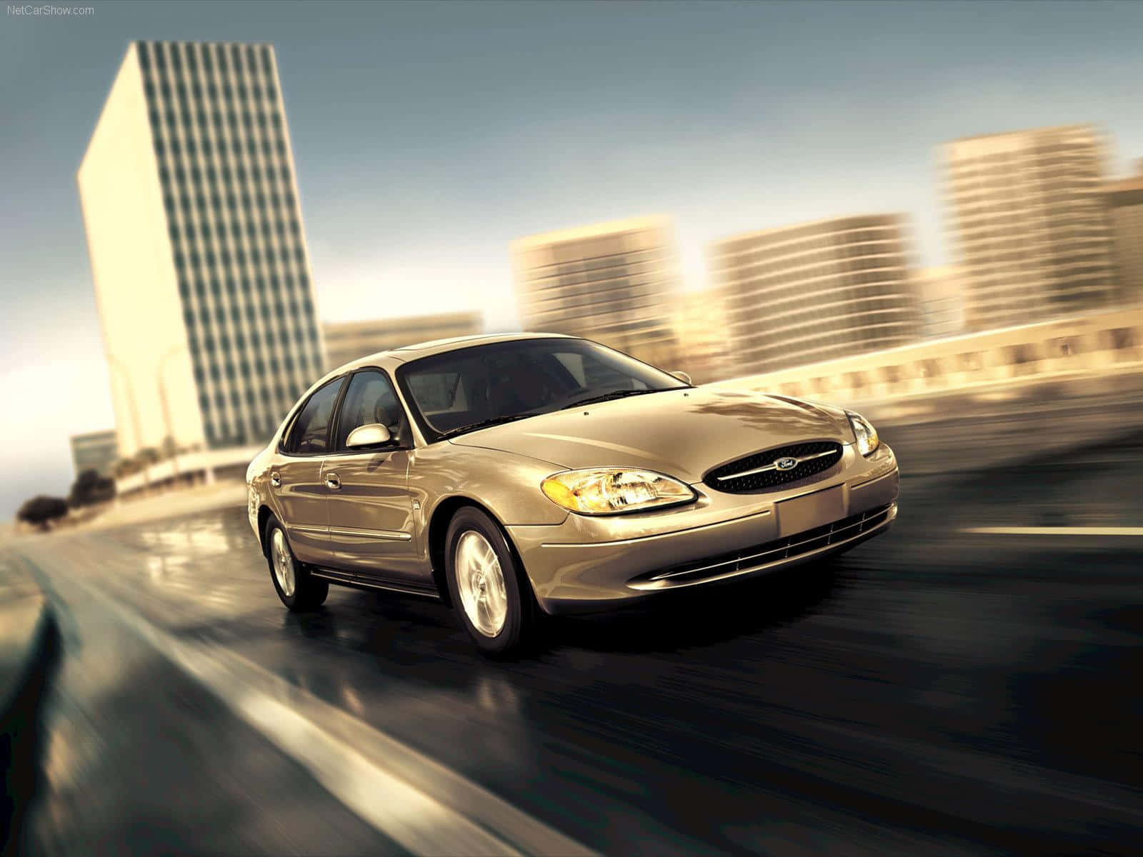 Ford Taurus 桌布 壁紙 — 一輛金色轎車在潮濕的城市高速公路上疾馳，背景是模糊的摩天大樓，天空朦朧。