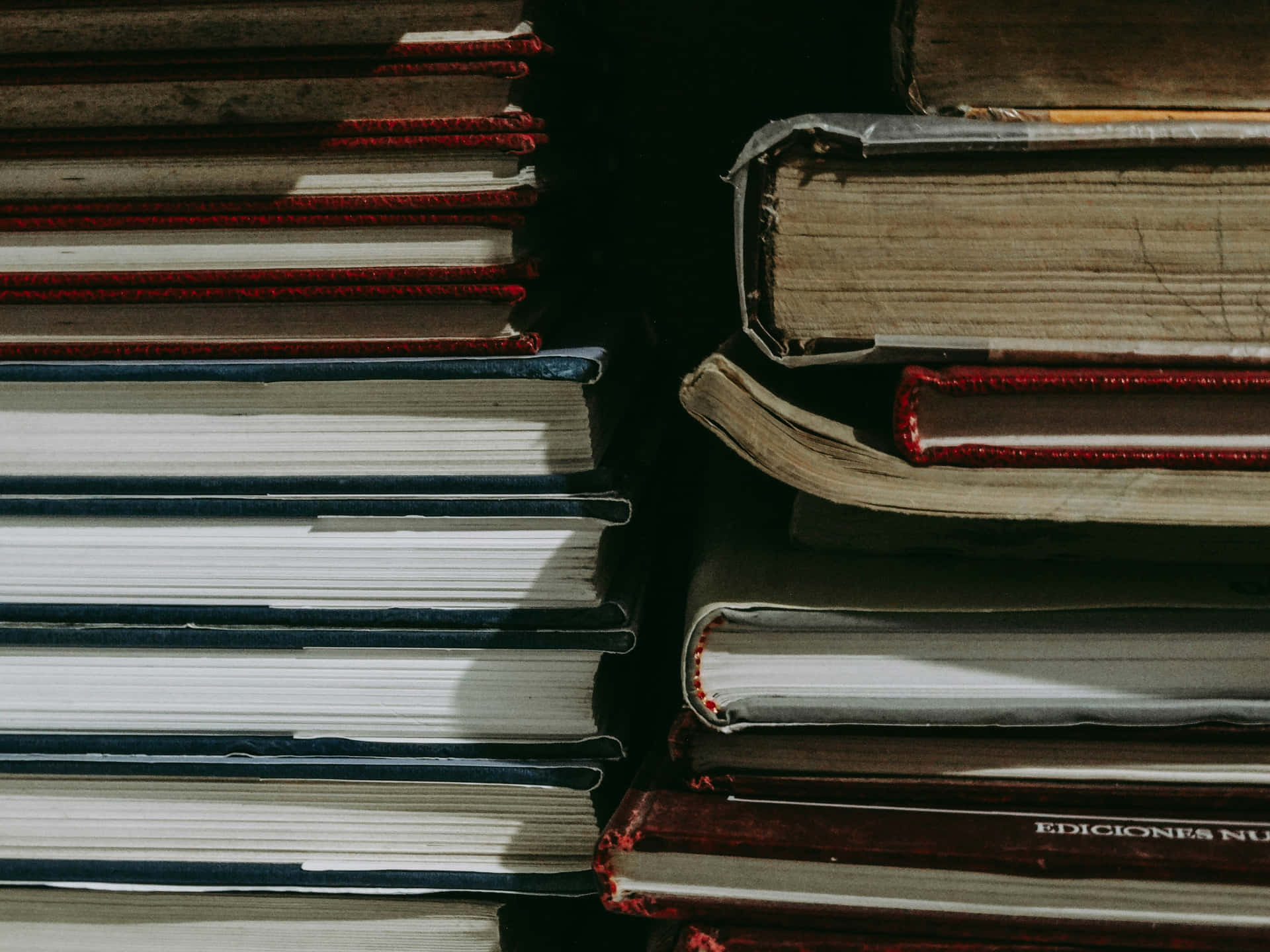  壁紙 — 一堆紅色和藍色書脊的復古書籍，在黑暗背景下被戲劇性的側光照亮。