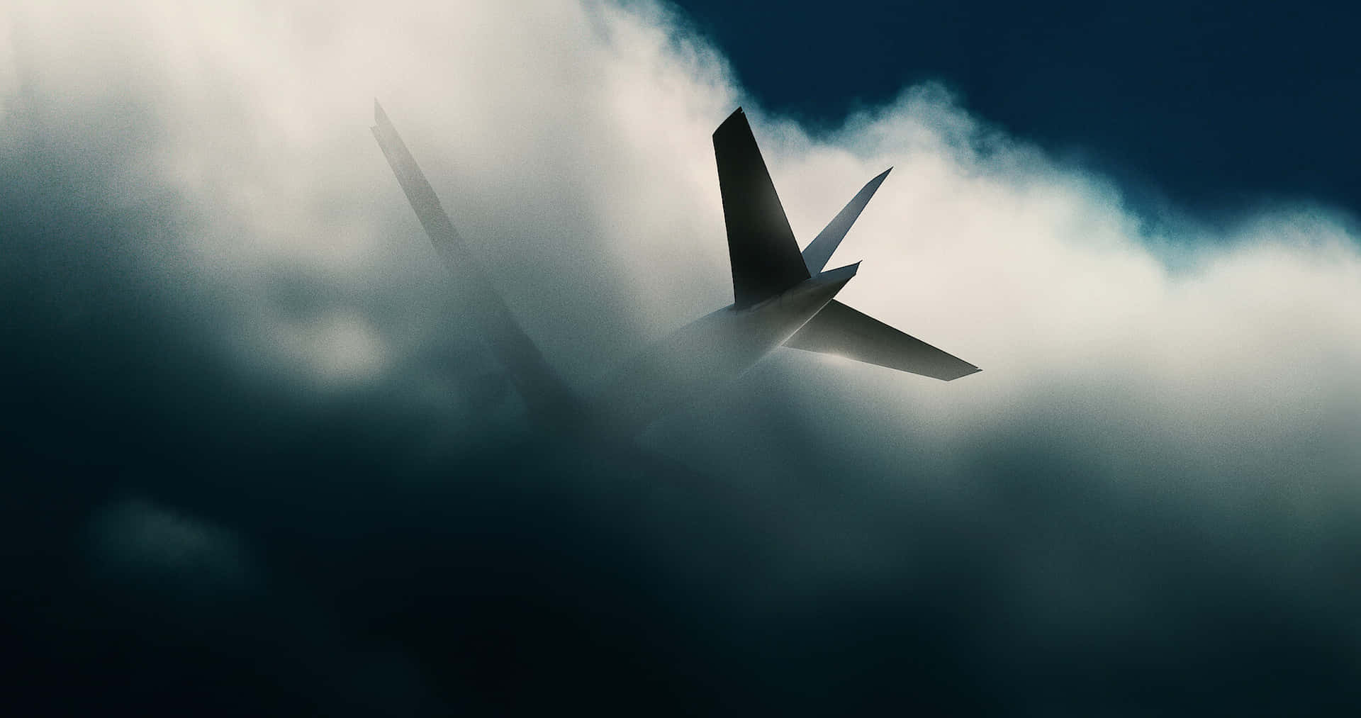  壁紙 — 一架流線型飛機的剪影在深藍色天空的戲劇性雲層中翱翔。