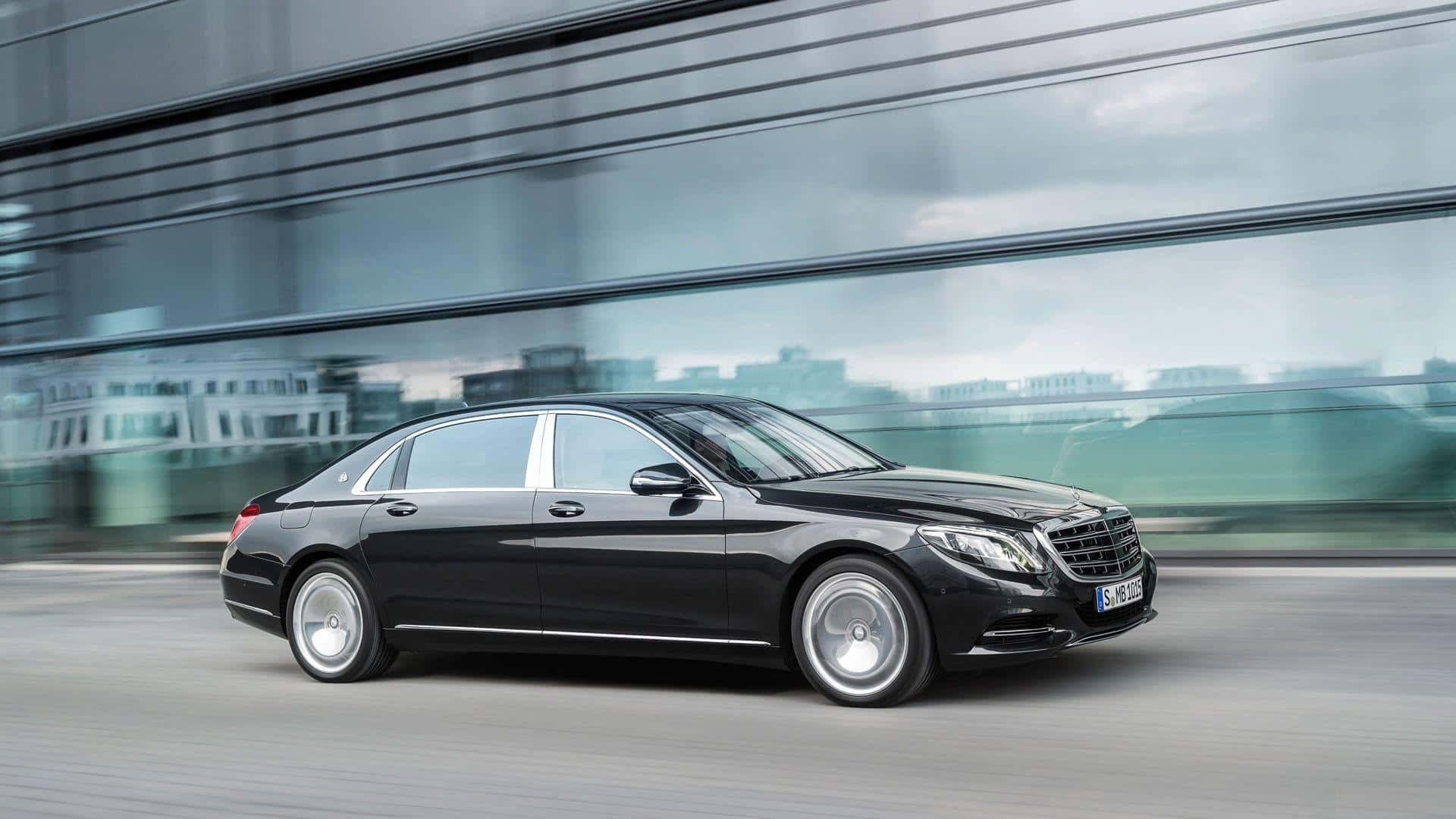 Maybach 桌布 壁紙 — 一架流線型黑色平治S-Class房車在現代都市環境中快速滑行，背景是模糊的玻璃建築。