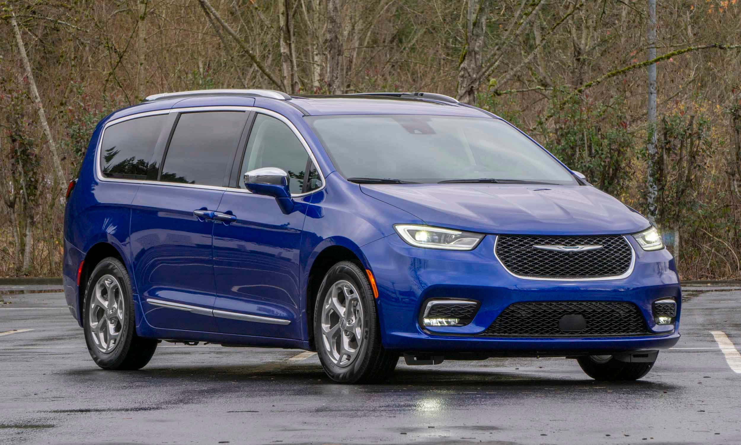 Chrysler Pacifica 桌布 壁紙 — 一架亮藍色嘅Chrysler Pacifica小型貨車停喺濕瀝青停車場，背景有光禿禿嘅樹。