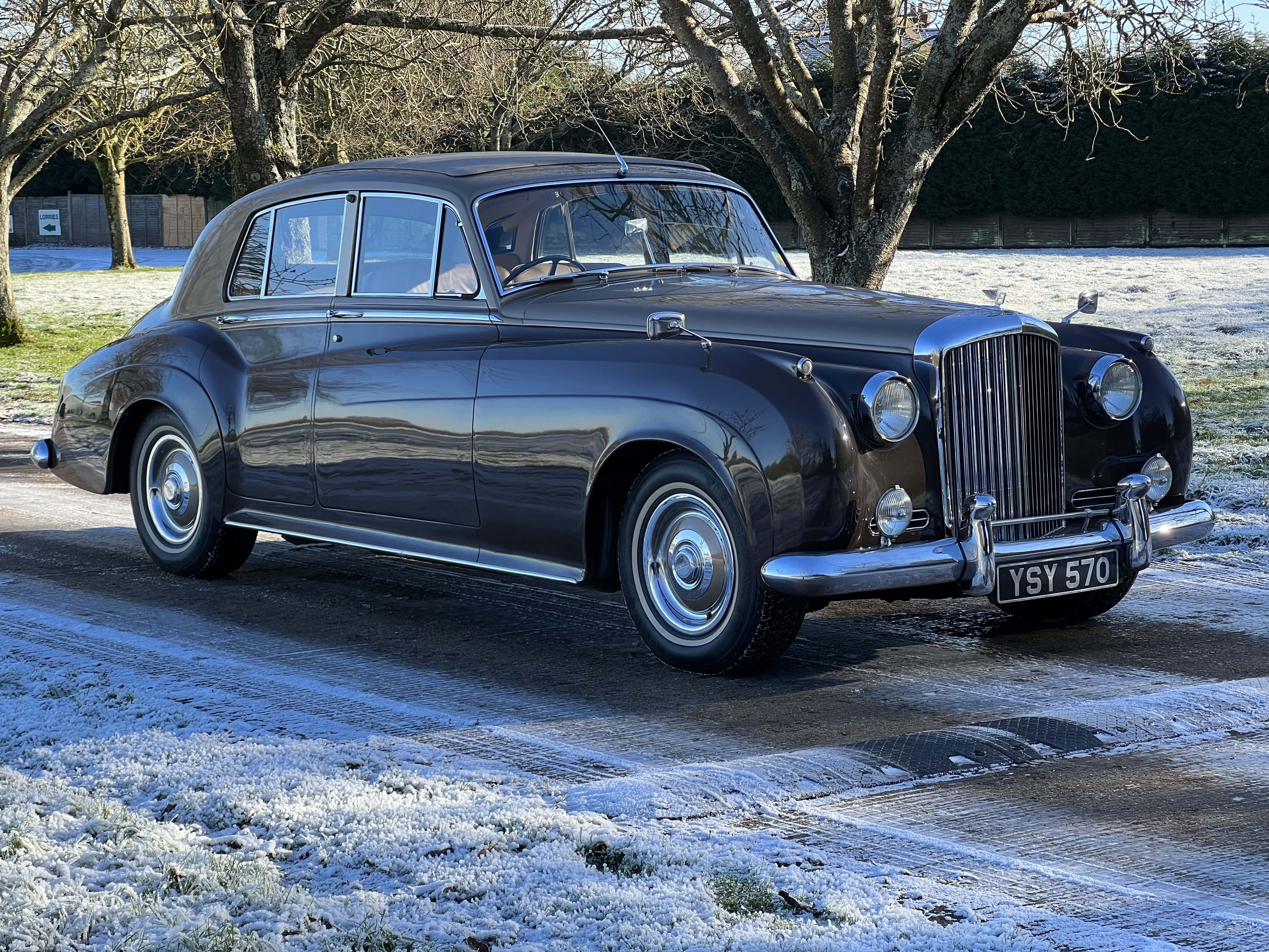 Bentley S2 桌布 壁紙 — 一架時尚嘅 vintage Bentley 房車喺冬日陽光下，喺鋪滿霜嘅車道上，喺光禿禿嘅樹旁邊閃閃發光。
