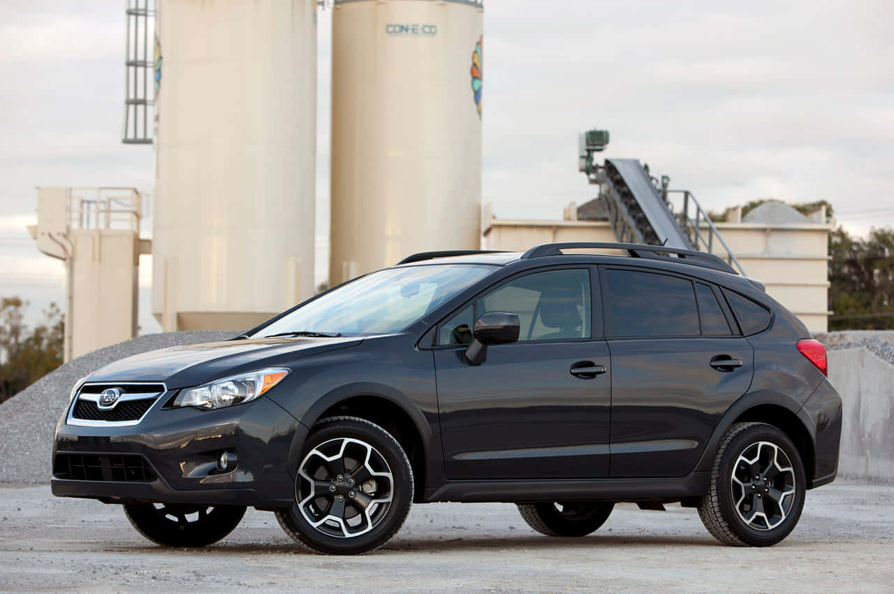 Fiat Tipo 桌布 壁紙 — 一架時尚深灰色 Subaru Crosstrek SUV 停泊在碎石上，靠近大型工業筒倉，天空多雲。