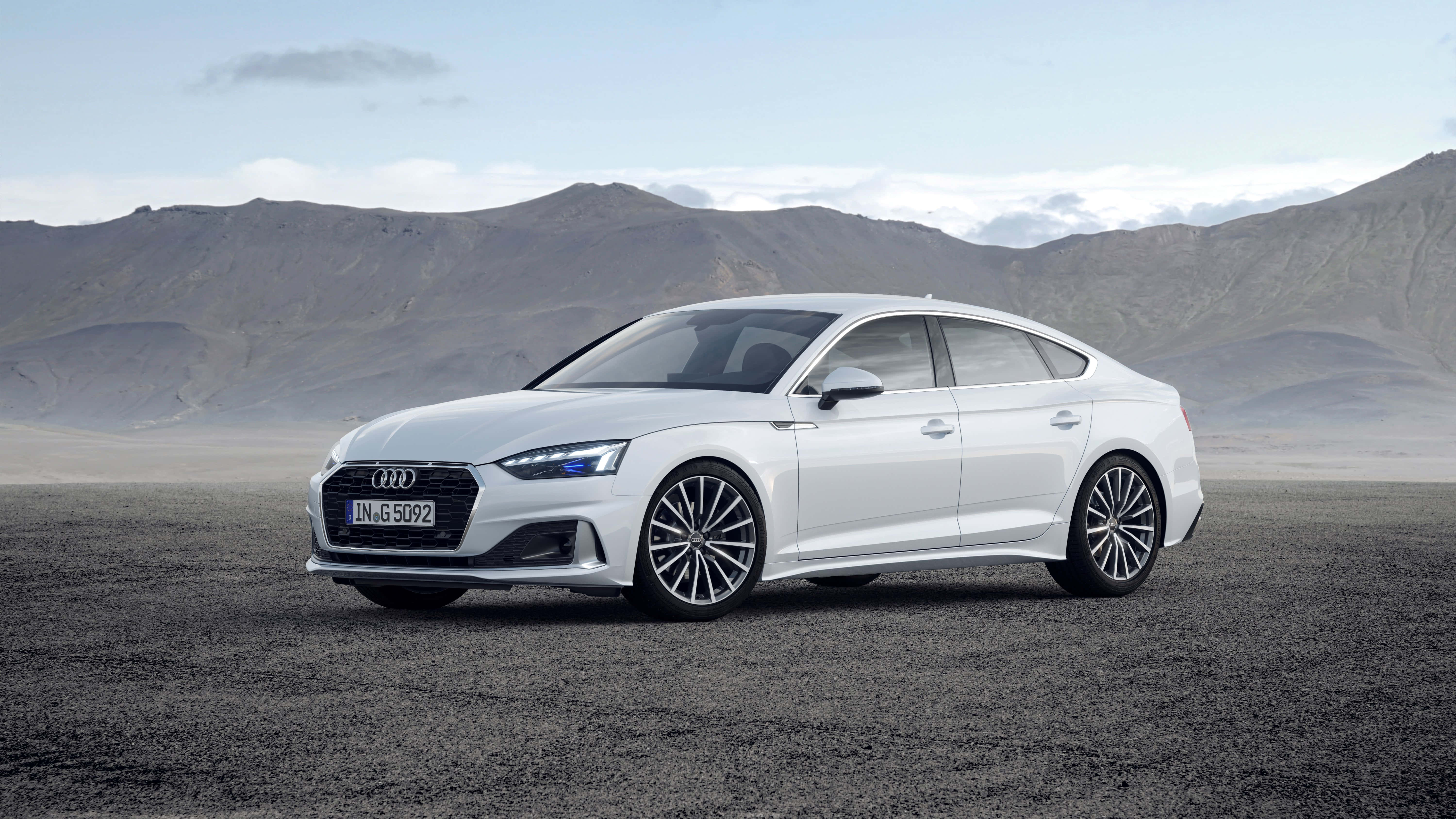 Audi A5 桌布 壁紙 — 一架時尚的白色Audi房車停泊在碎石平原上，背景是蒼白天空下的崎嶇山脈。