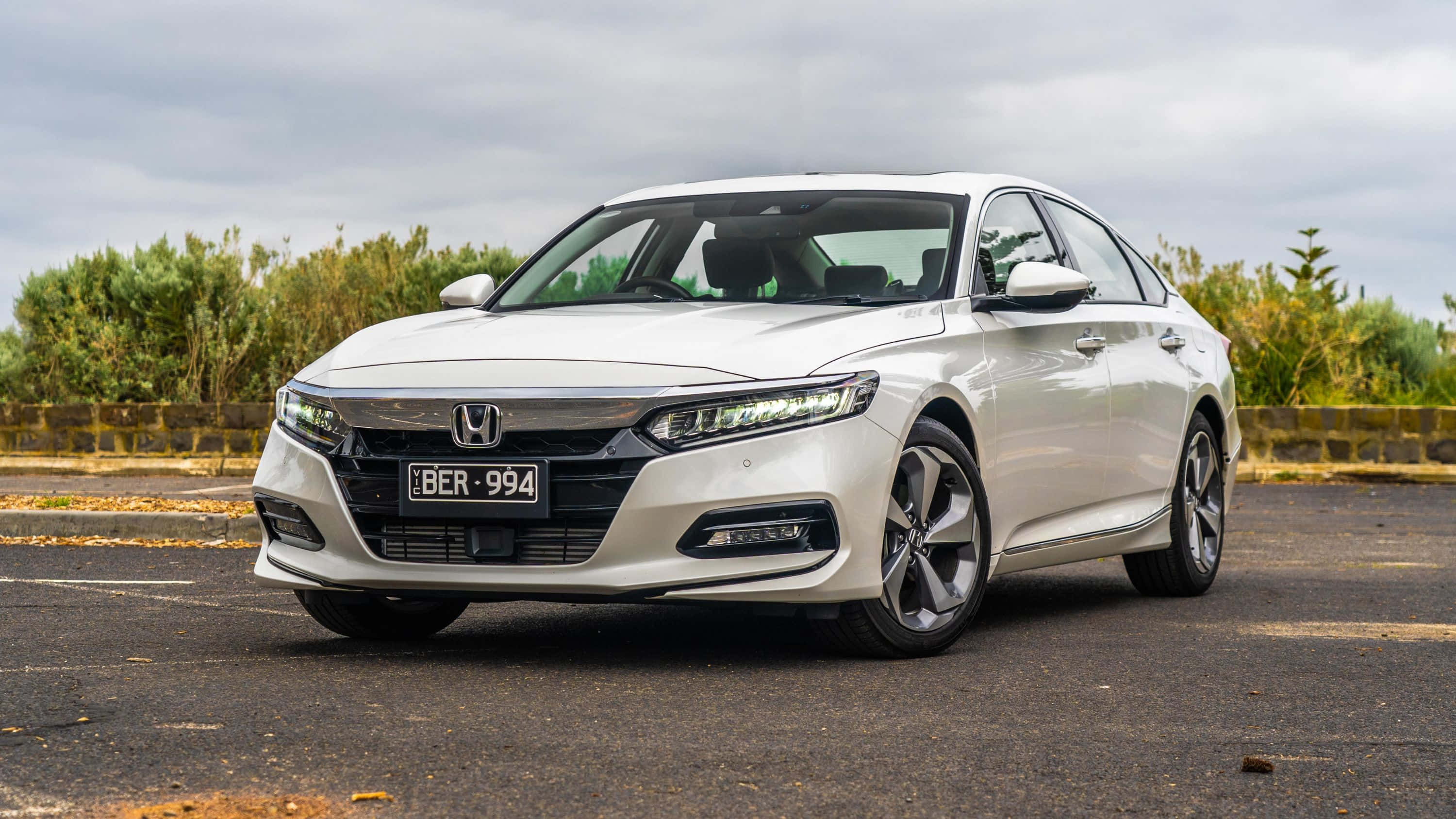 Honda Accord 桌布 壁紙 — 一架時尚的白色本田雅閣房車停在瀝青路上，背景有綠色灌木叢和陰天。