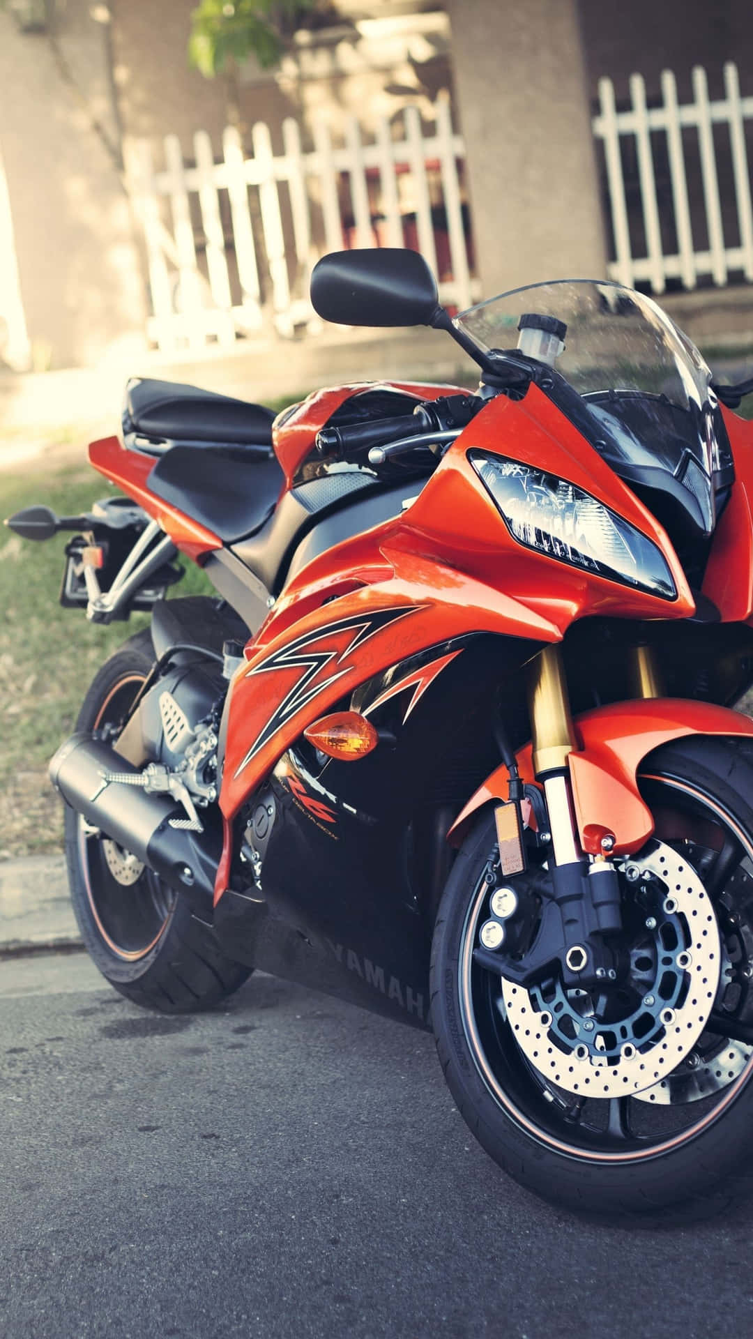  壁紙 — 一架鮮橙色和黑色的Yamaha運動電單車停泊在街道上，旁邊有白色柵欄，在柔和日光下。