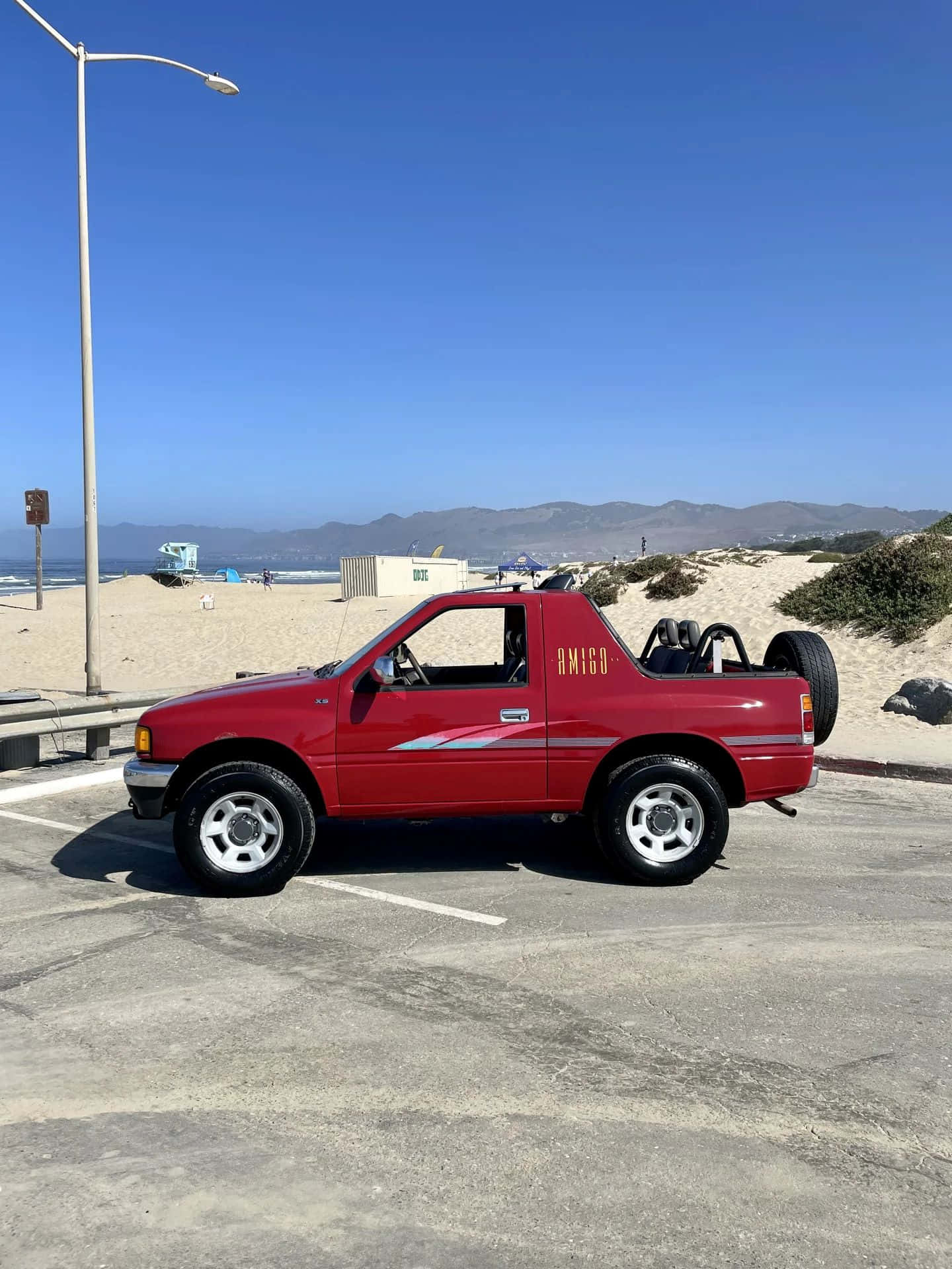  壁紙 — 一架鮮紅色的沙丘越野車停泊在陽光明媚的海邊停車場，背景有山脈和海洋。