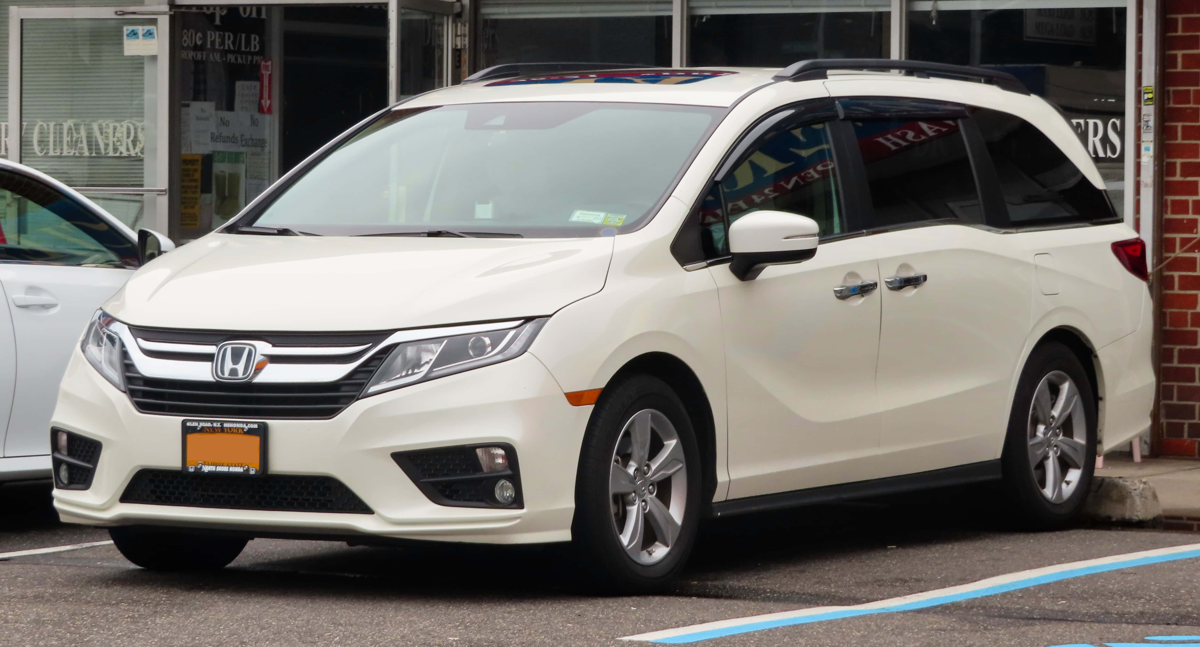 Honda Odyssey 桌布 壁紙 — 一架乾淨的白色本田Odyssey小型貨車停泊在城市地塊，旁邊有一棟磚建築和另一輛車。