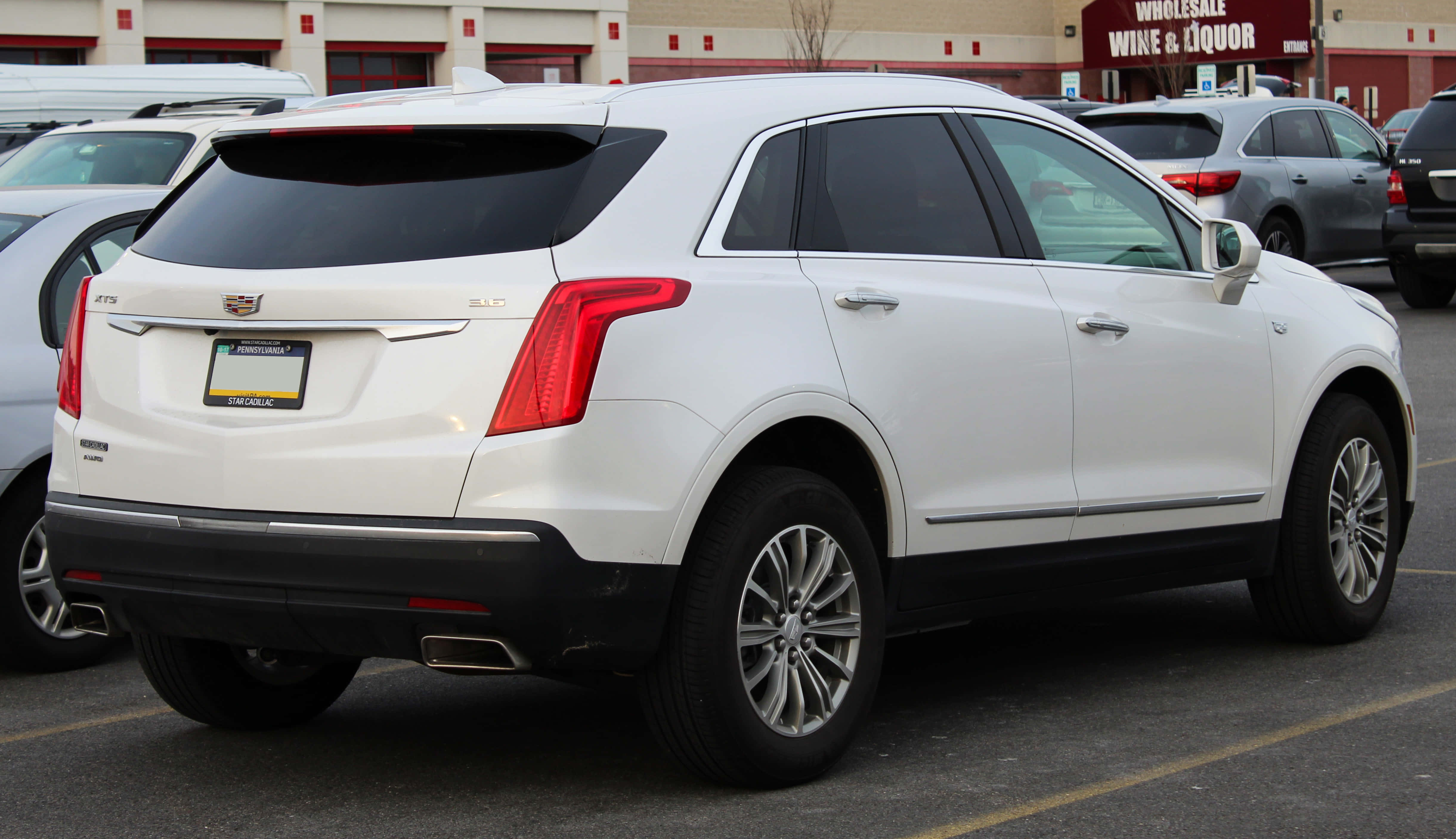 Cadillac Xt5 桌布 壁紙 — 一架純白色嘅Cadillac XT5 SUV停泊喺商業停車場，背景有其他車輛同一間批發酒舖。