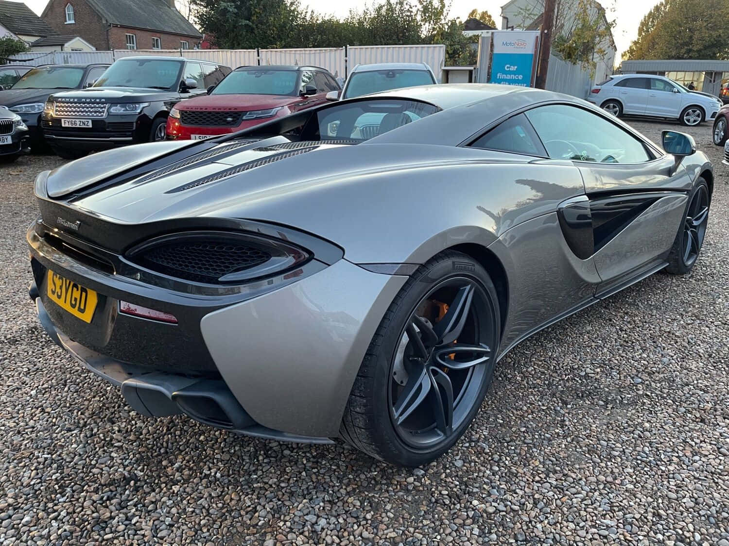 Mclaren 540c 桌布 壁紙 — 一架型格銀色McLaren 570S跑車停泊在碎石地上，背景有其他車輛。