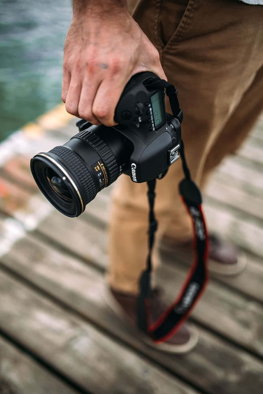Cameraman 桌布 壁紙 — 一個人喺水邊嘅木碼頭上，手持一部黑色Canon DSLR相機，配有大鏡頭。