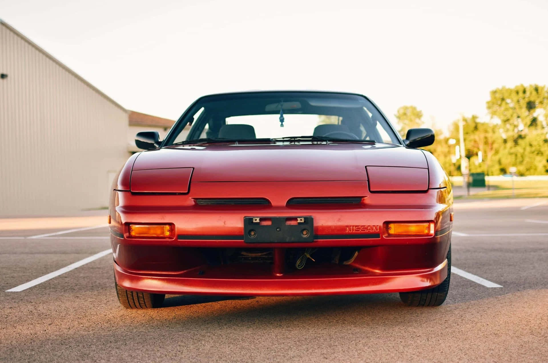  壁紙 — 一架亮紅色日產240SX跑車停泊在停車場，帶有溫暖的日落燈光。