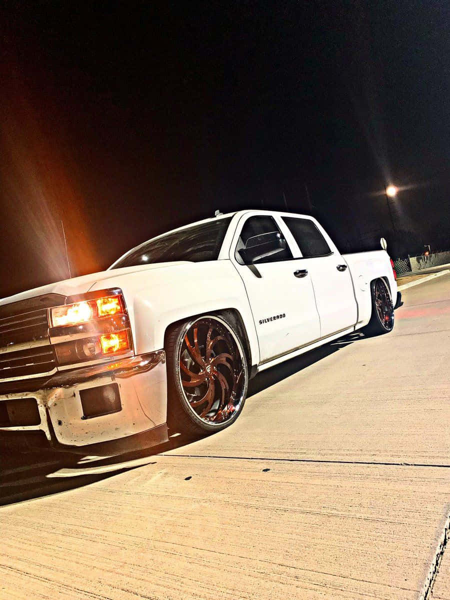  壁紙 — 一輛白色升高嘅Chevrolet Silverado pickup truck，配備定制青銅輪圈，夜晚停泊喺混凝土場地，喺人造燈光下。