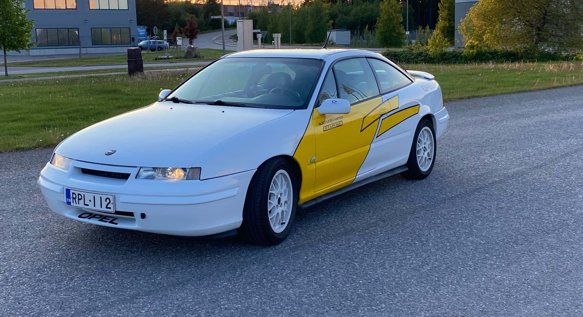 Opel Calibra 桌布 壁紙 — 一輛白色和黃色的歐寶運動型轎跑車停泊在日落時分的碎石路上，背景有建築物和樹木。