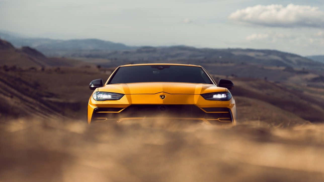 Lamborghini Urus 桌布 壁紙 — 一輛充滿活力的黃色林寶堅尼在塵土飛揚的田野中疾馳，背景是起伏的丘陵和多雲的天空。