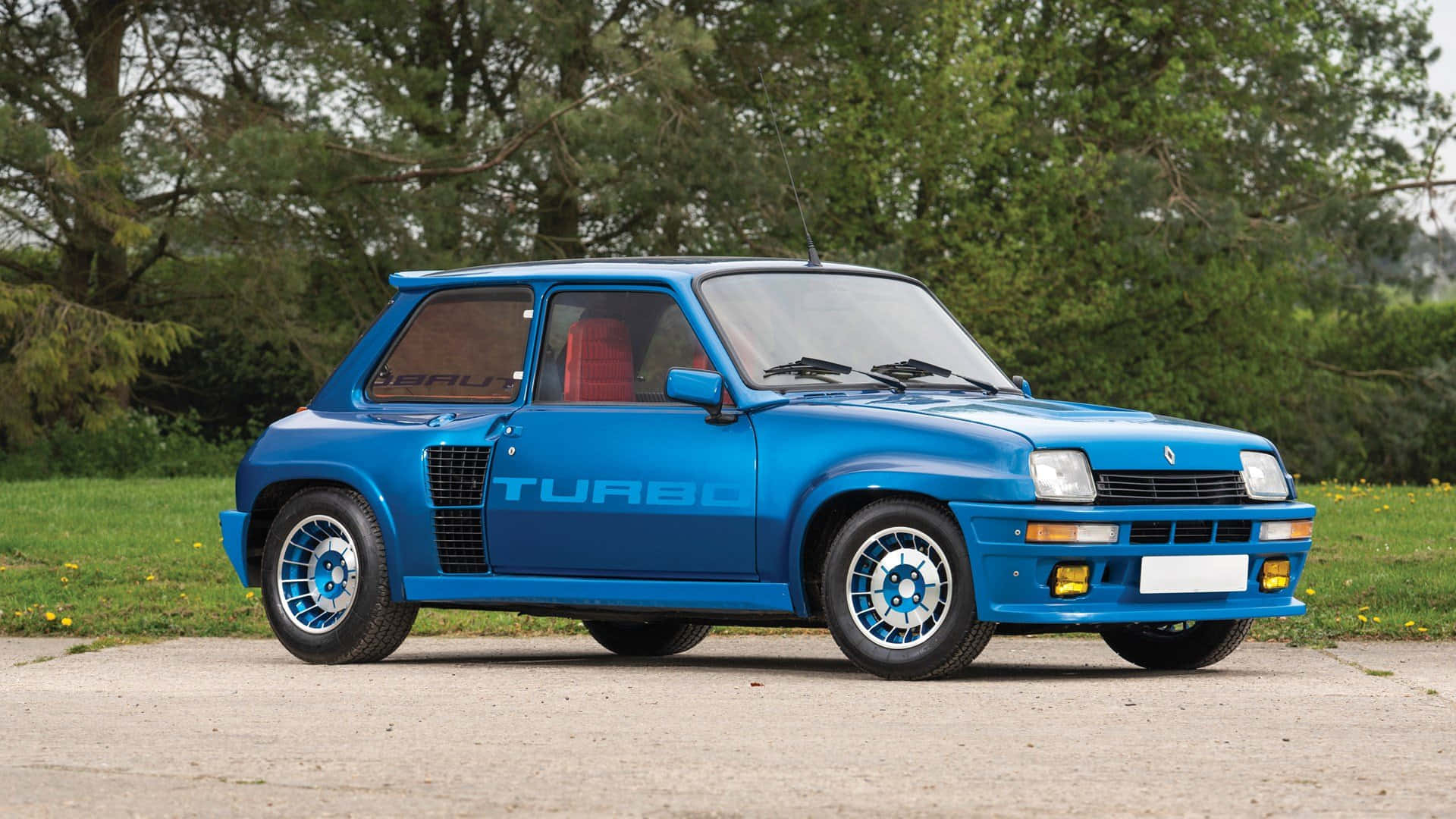 Renault 5 Turbo 桌布 壁紙 — 一輛充滿活力的藍色雷諾5 Turbo跑車停在碎石上，背景有綠樹和草地。