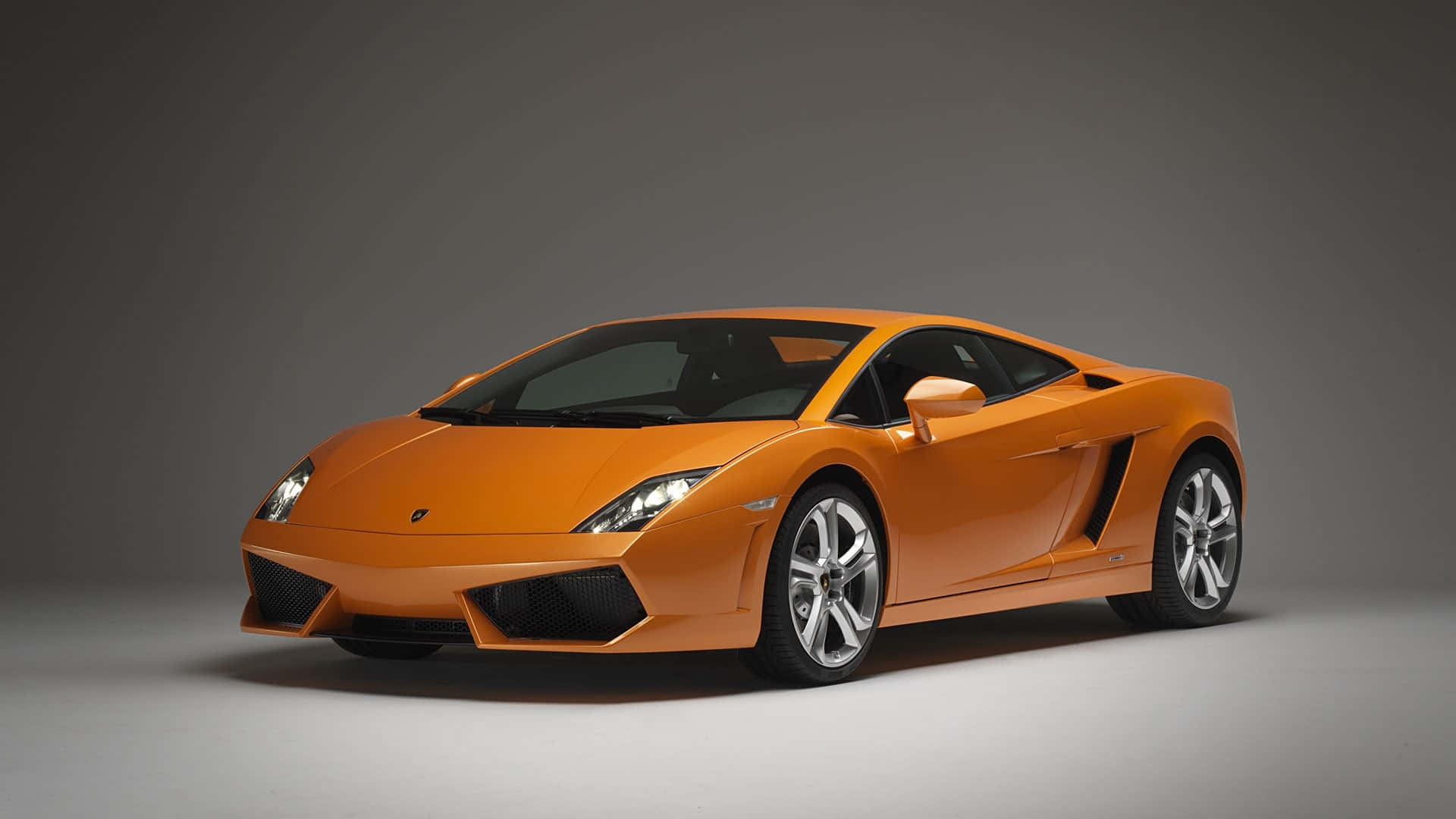 Lamborghini Gallardo 桌布 壁紙 — 一輛充滿活力的橙色林寶堅尼Gallardo跑車以四分之三角度擺放在中性灰色工作室背景前。