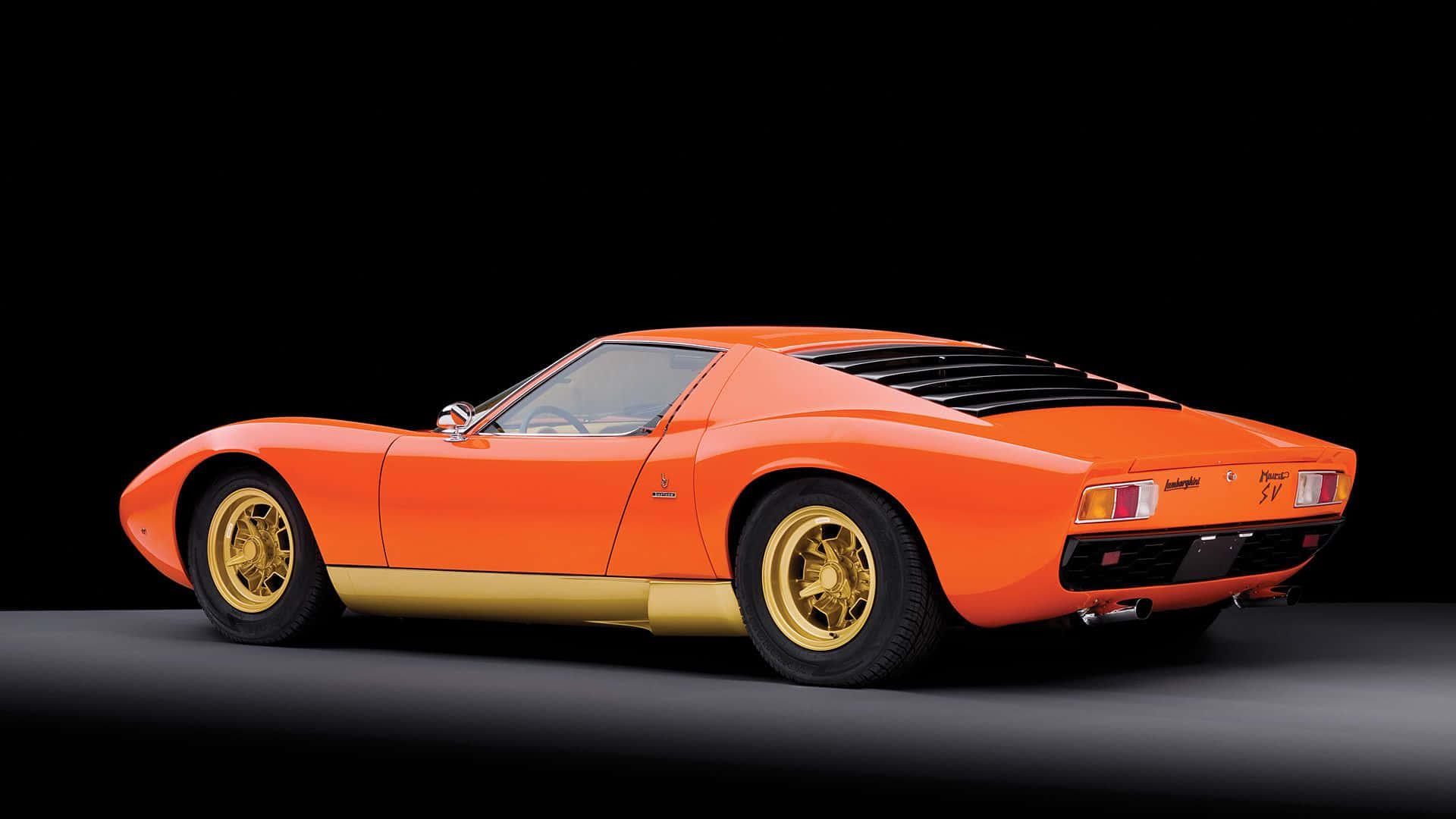 Lamborghini Miura 桌布 壁紙 — 一輛充滿活力的橙色林寶堅尼Miura跑車，配備金色飾件和輪圈，在黑色背景的攝影棚中展示。