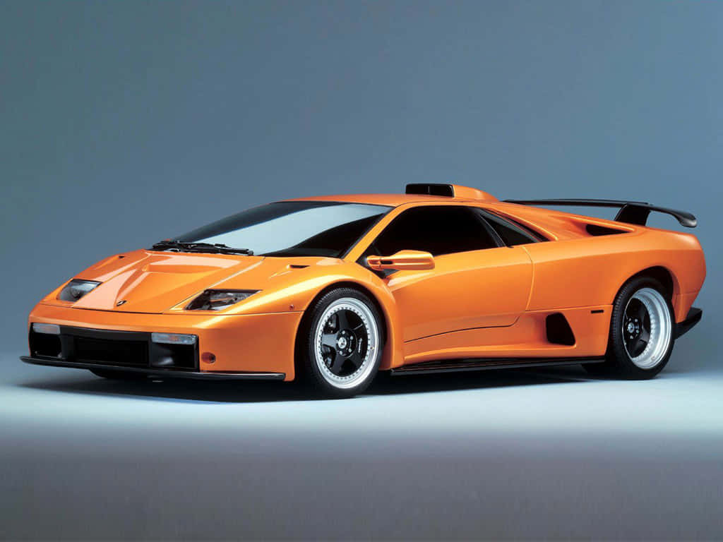 Lamborghini Diablo 桌布 壁紙 — 一輛充滿活力的橙色林寶堅尼 Diablo SV 跑車，帶有黑色飾邊和銀色輪圈，在灰色漸變工作室背景前擺拍。